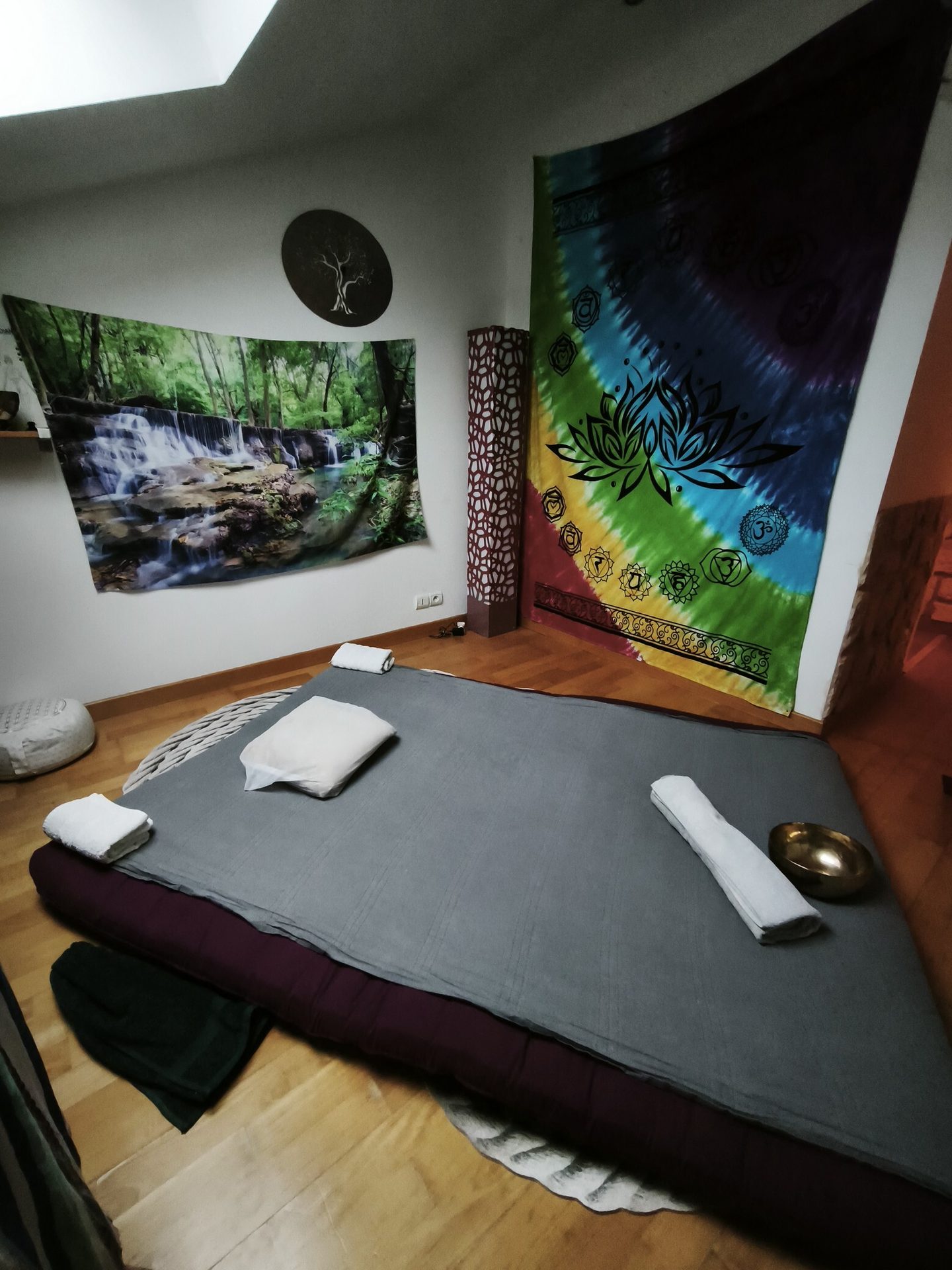 A tranquil room with a floor mattress, waterfall and chakra tapestries, and a singing bowl.