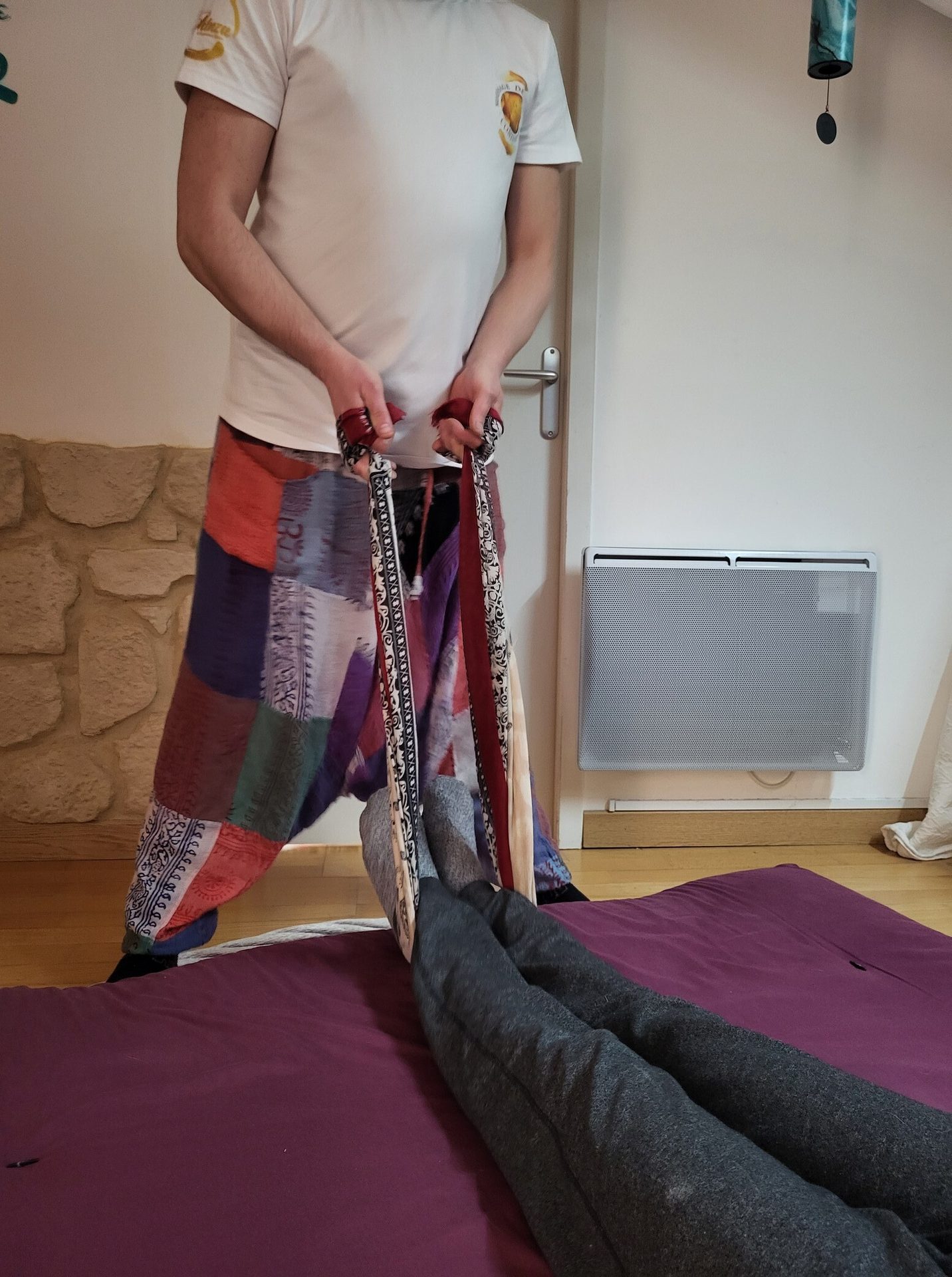 Person in patchwork pants holds straps connected to feet lying on mat for bodywork.