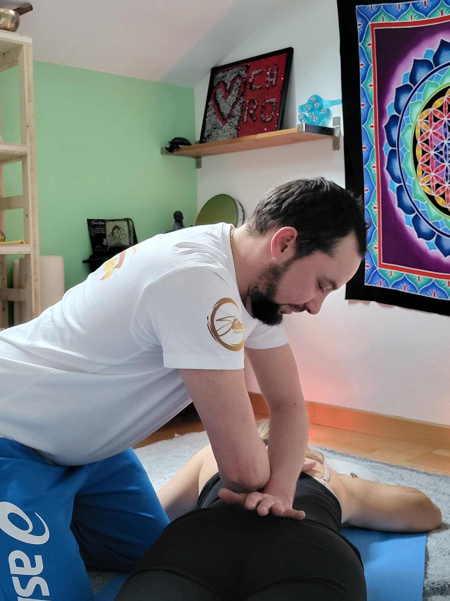 A man massages a woman's back with his elbow on a blue mat.