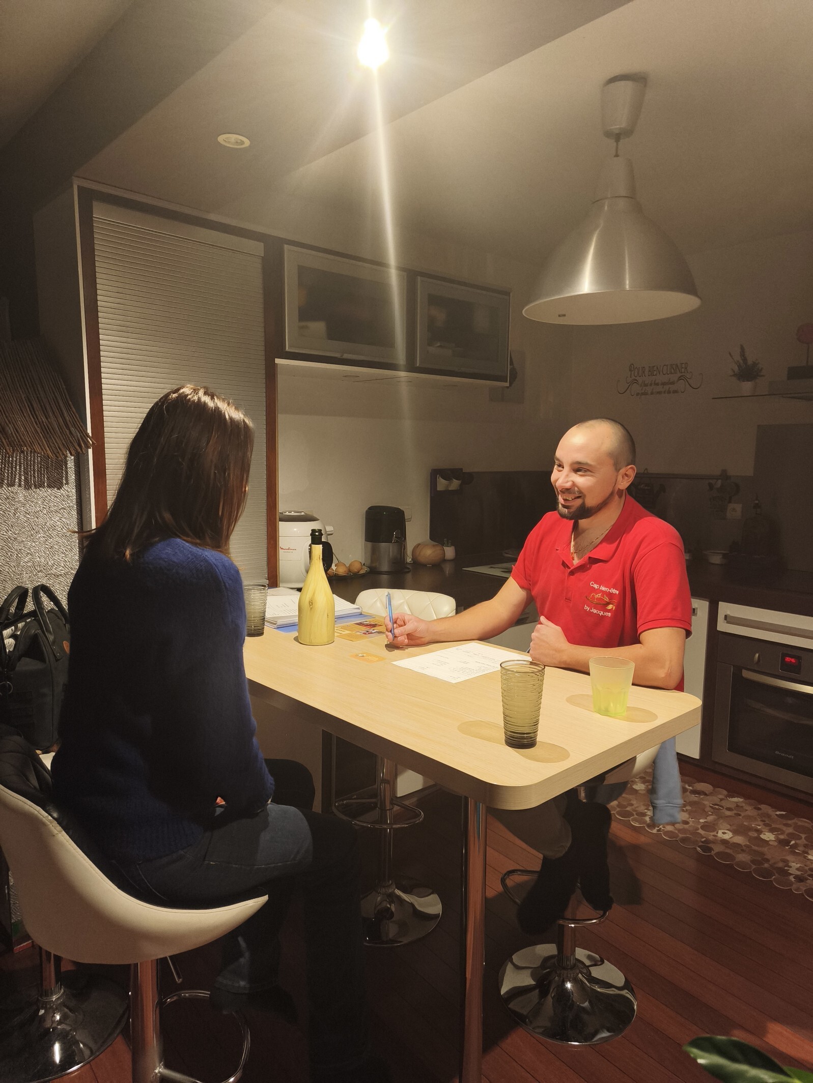 A smiling man and a woman sit at a kitchen island, appearing to be in a discussion or meeting.