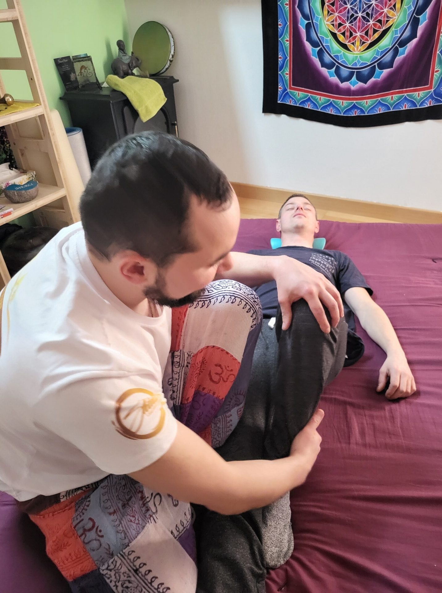 Therapist performs leg therapy on a client lying on a mat. Colorful room decor.