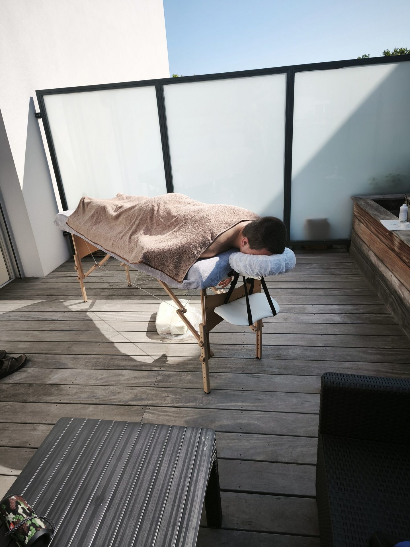 Man relaxing on an outdoor massage table on a sunny wooden deck.