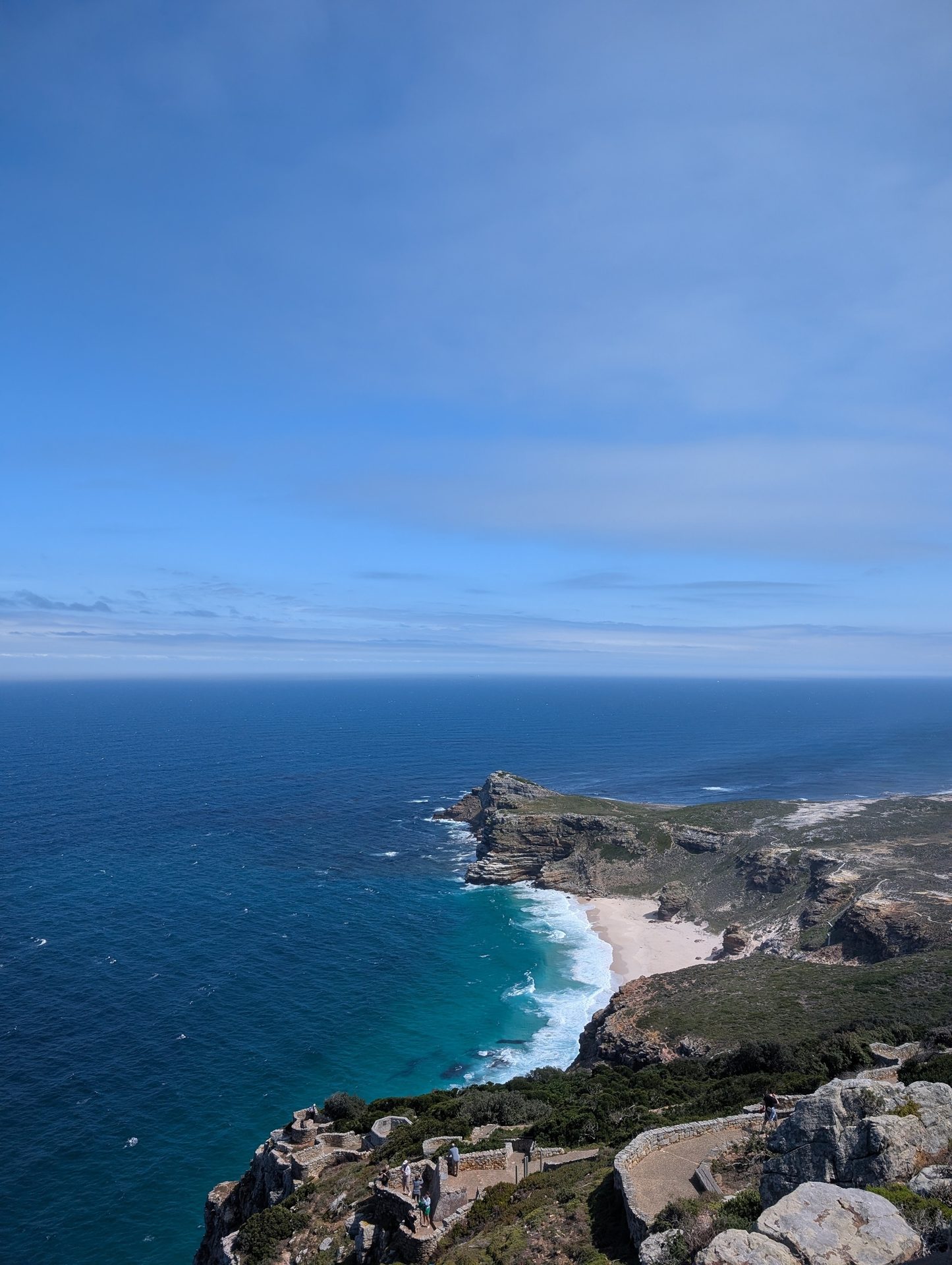 A dramatic high-angle view of a rugged coastline with a white sand beach and turquoise ocean.