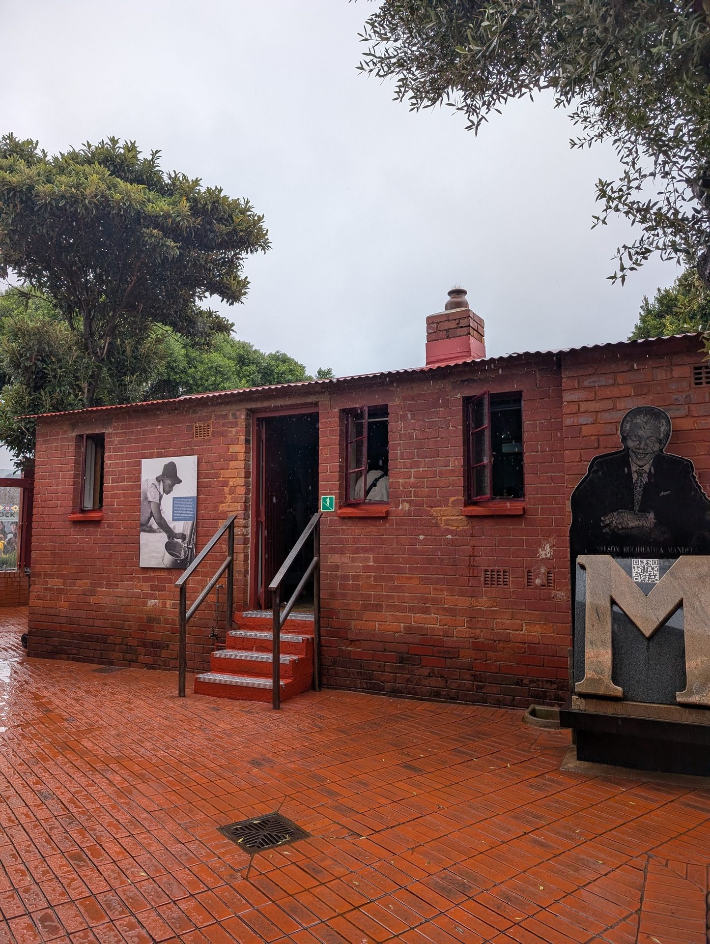 Red brick house, Nelson Mandela monument, and wet tiled ground on a rainy day.