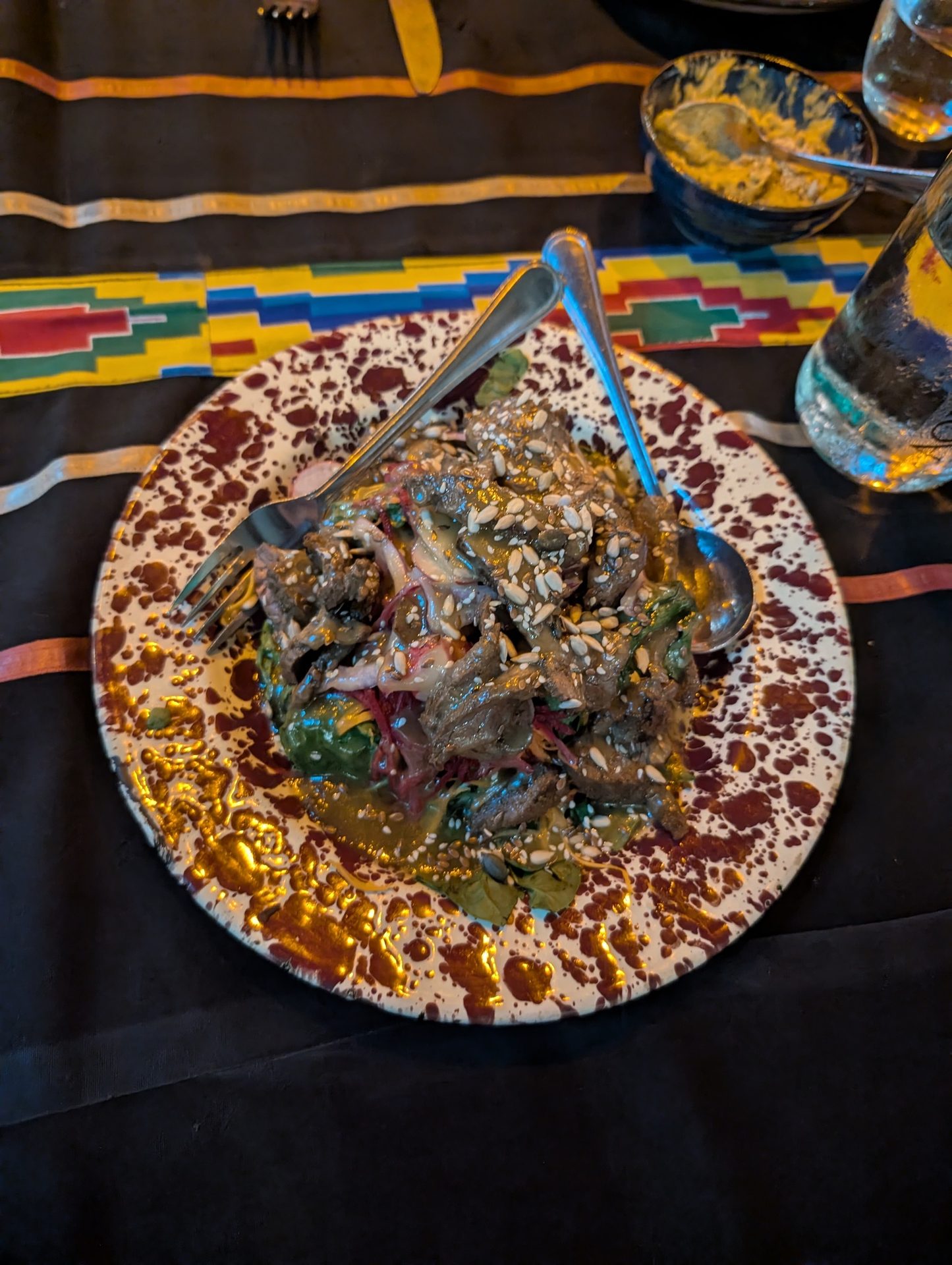 A delicious dish featuring a meat and vegetable salad topped with seeds on a speckled plate.