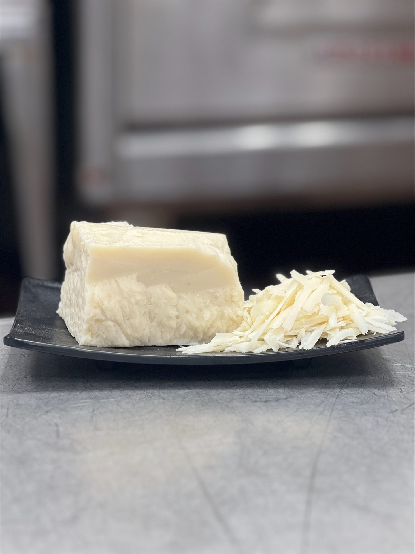 A block of white cheese or butter and a pile of shredded flakes on a black plate.