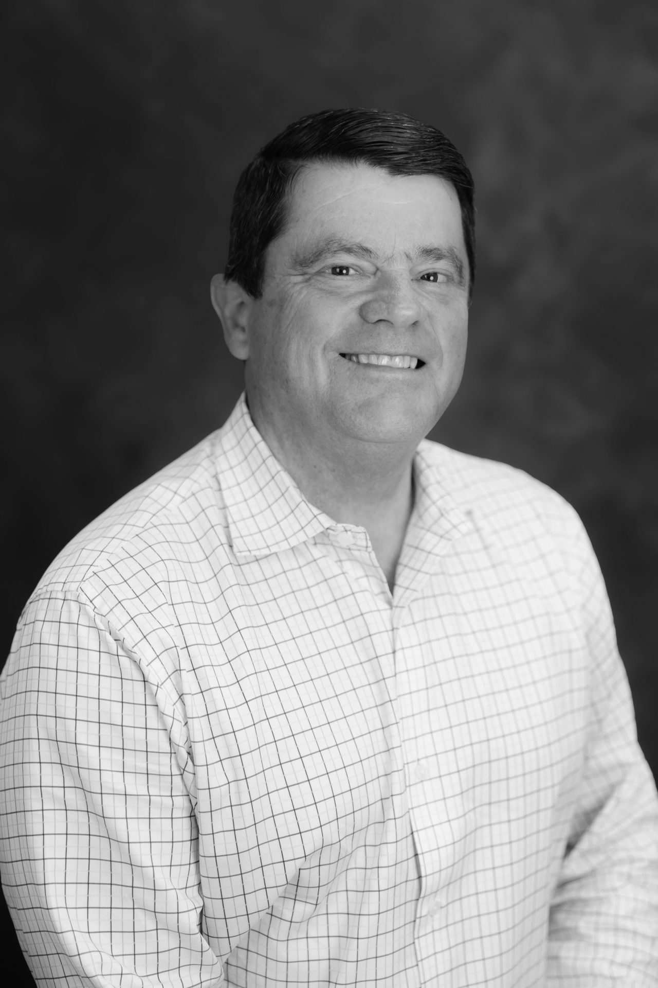 Black and white portrait of a smiling man in a checkered shirt.