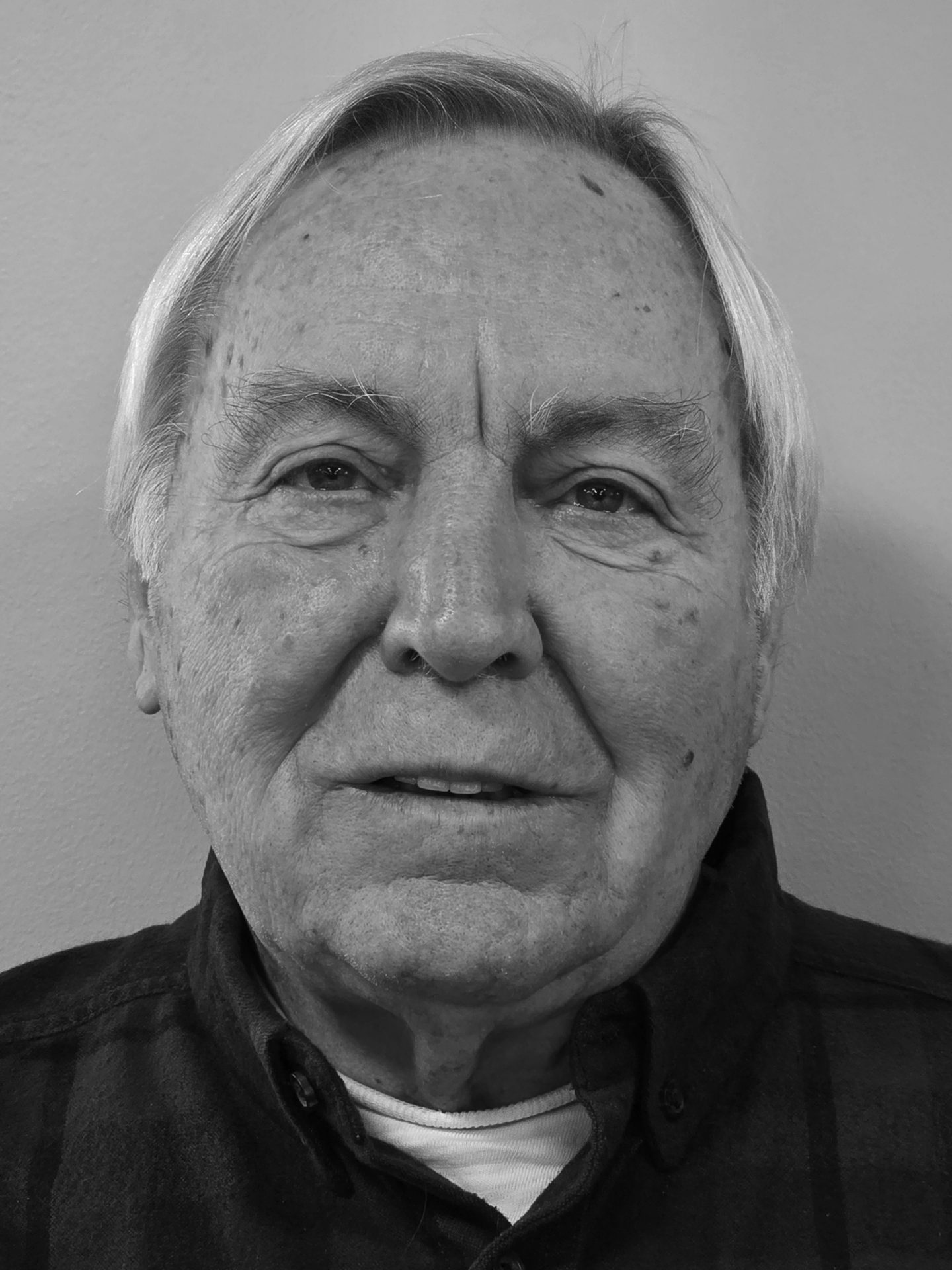 Black and white close-up portrait of an elderly man with white hair, looking directly at the camera.
