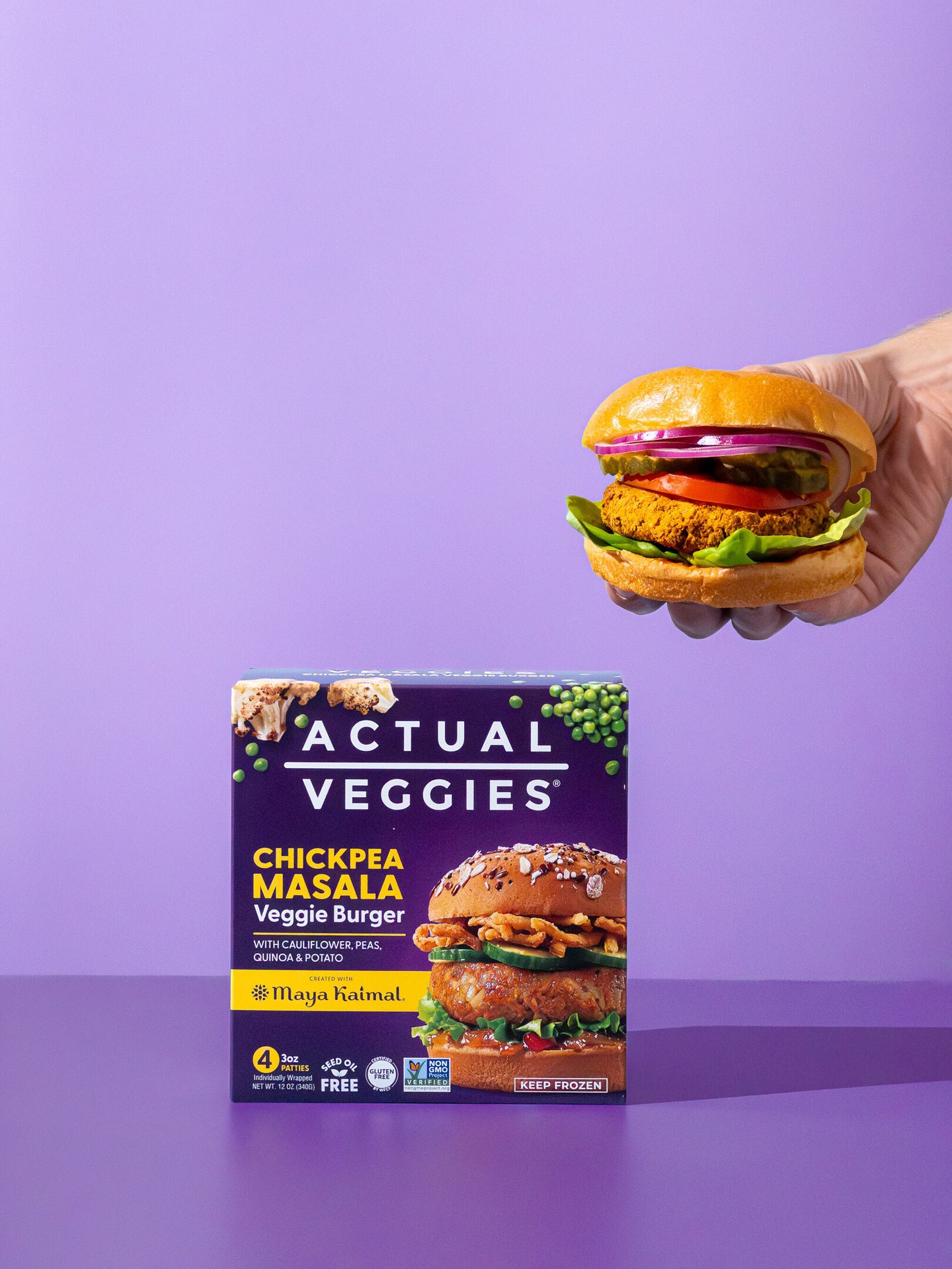 A box of Actual Veggies Chickpea Masala Veggie Burgers next to a prepared burger held in a hand.