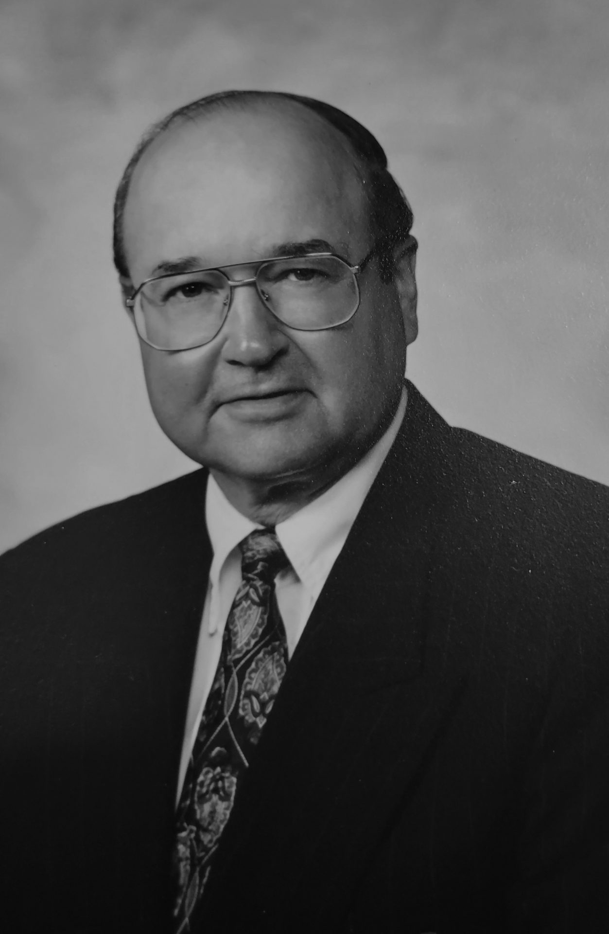 Black and white portrait of an older man wearing glasses, a suit, and a patterned tie.