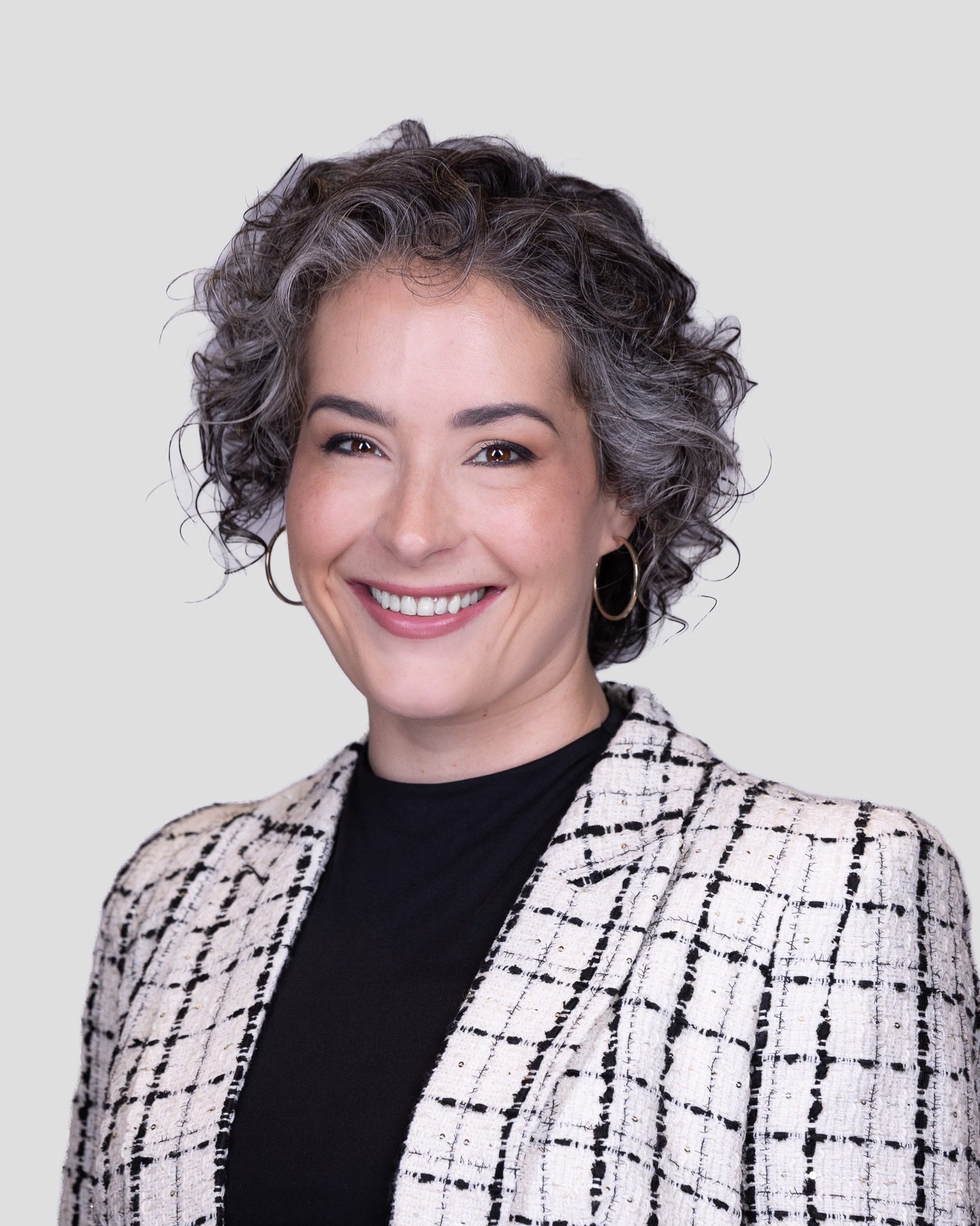 Smiling woman with short curly grey hair, gold hoop earrings, and a black and white checkered jacket.