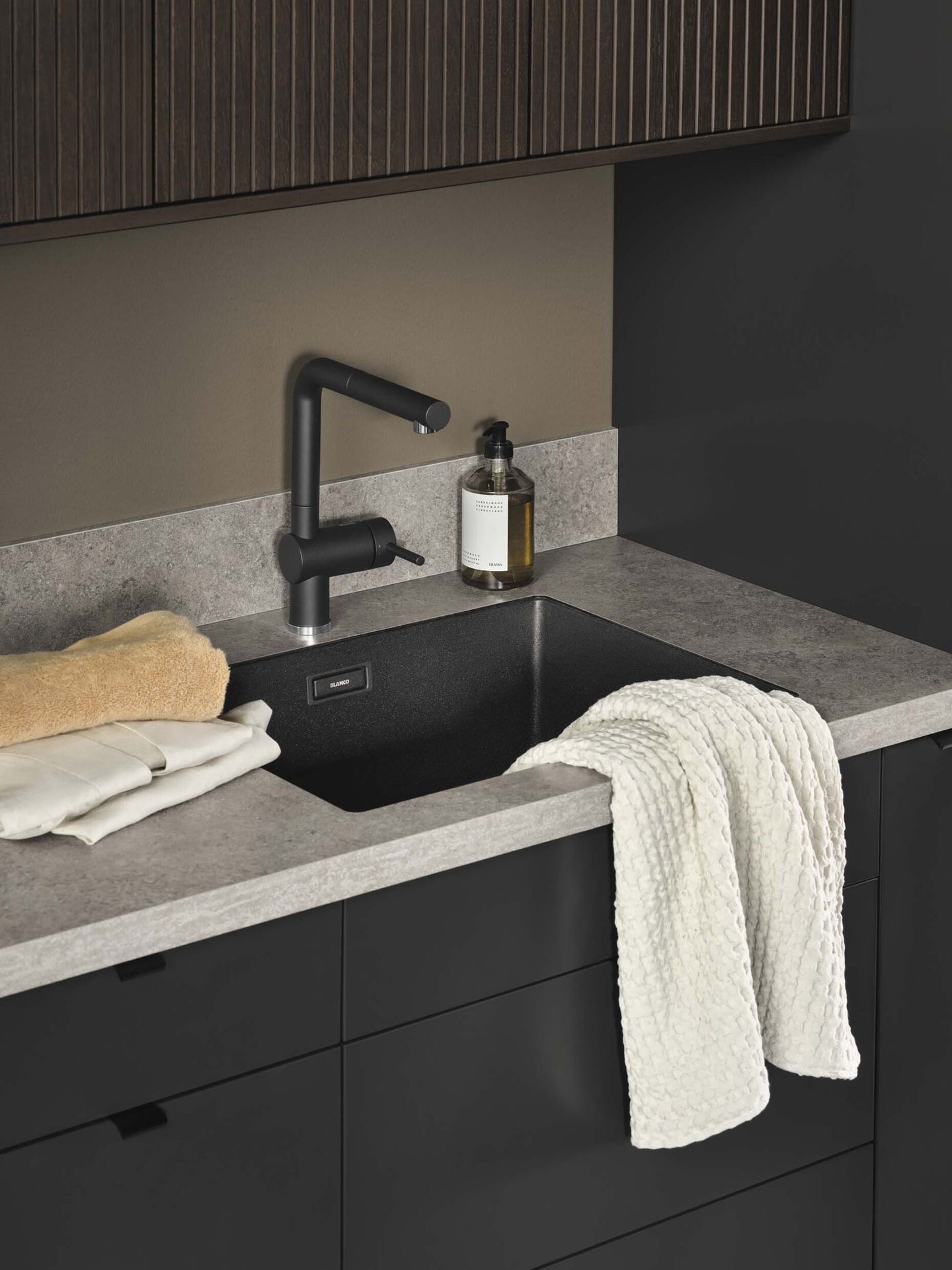 Modern black sink and faucet in a utility area with gray counter, dark cabinets, and towels.