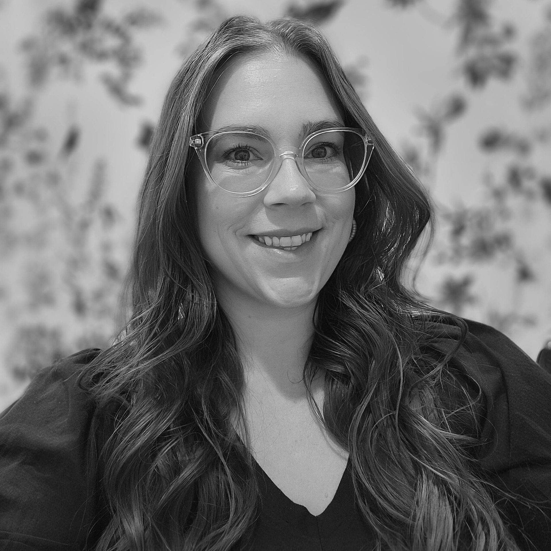 Black and white portrait of a smiling woman with long wavy hair and glasses.