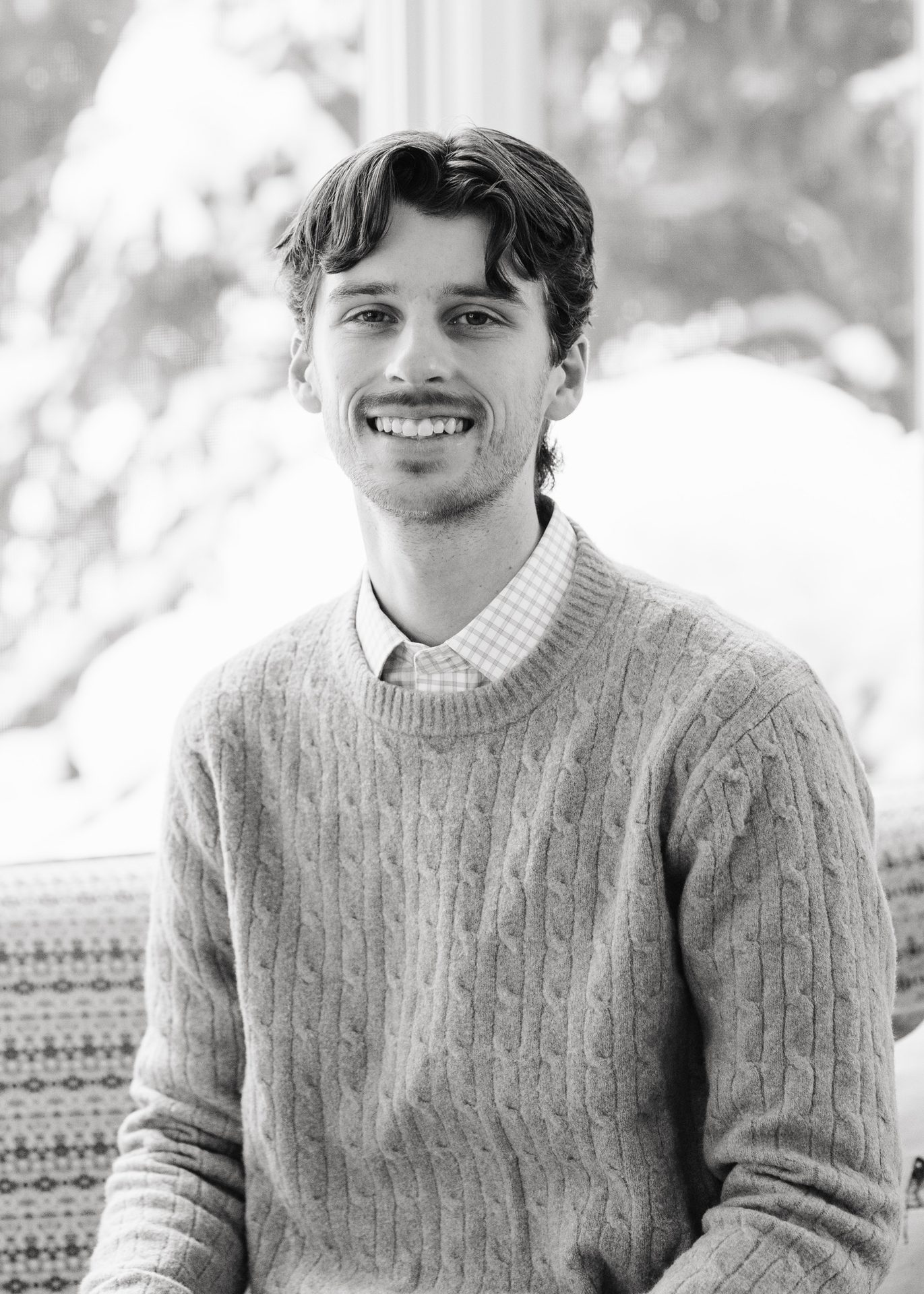 Black and white portrait of a smiling young man in a cable-knit sweater.