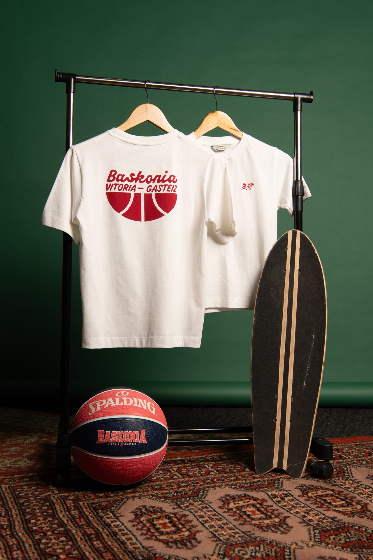 White Baskonia T-shirts on a rack with a Spalding basketball and skateboard on a patterned rug.