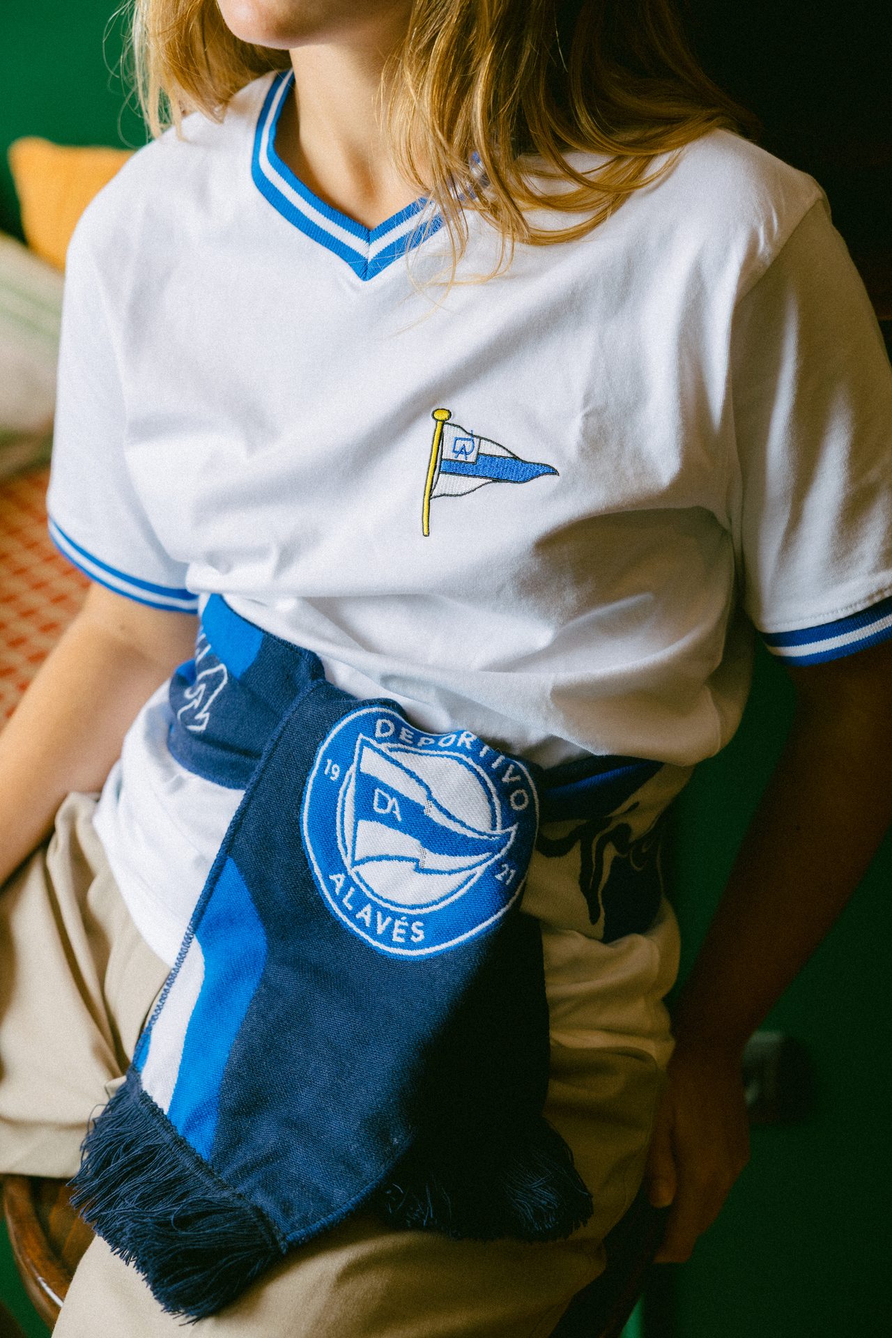 Person in white t-shirt with flag embroidery and blue Deportivo Alavés scarf.