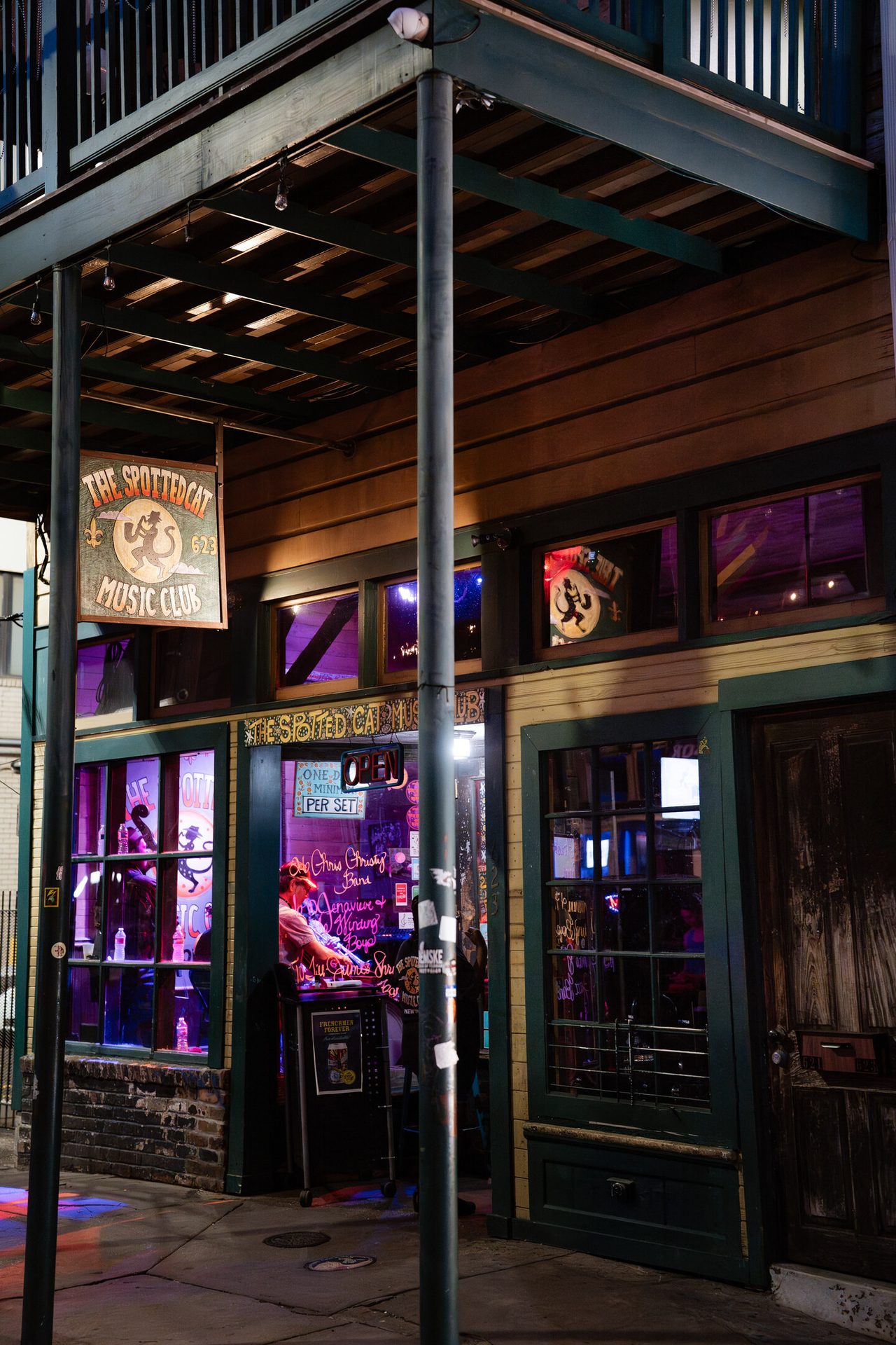 The Spotted Cat Music Club at night, with neon lights illuminating its entrance and hanging sign.