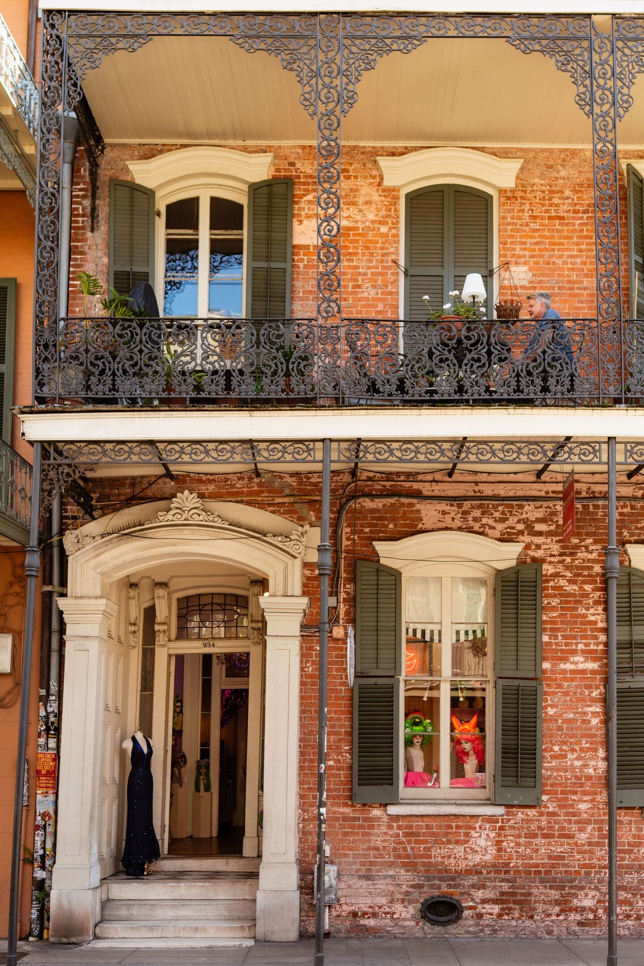 Historic brick building in New Orleans with ornate balconies, a man on the upper balcony, and street-level shops.
