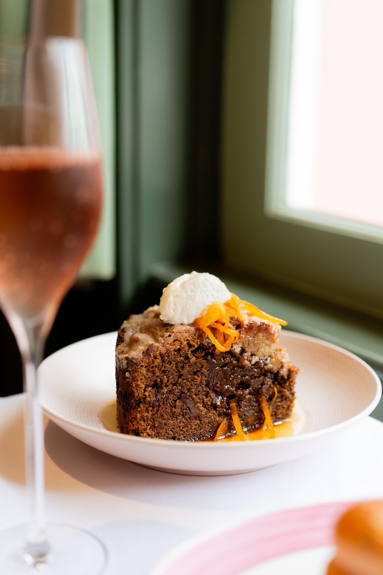 A decadent slice of cake with cream and orange zest, paired with a glass of sparkling rosé.