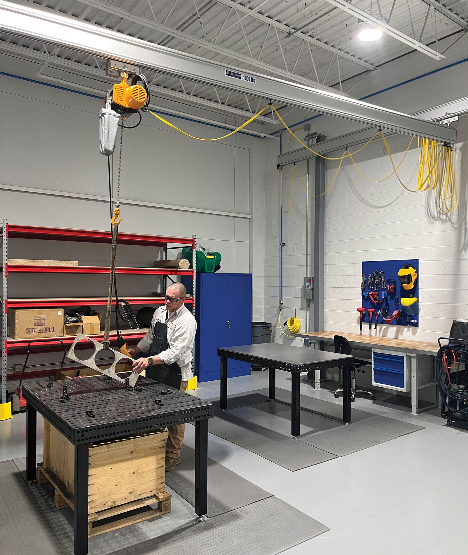 Worker in a modern workshop with an overhead crane handling a metal piece.