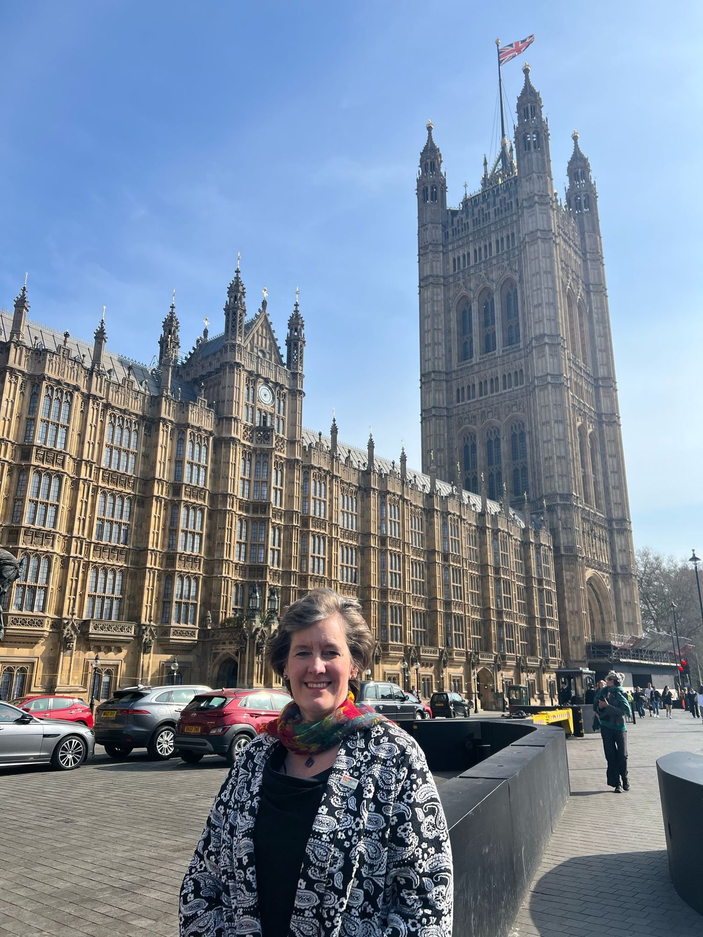 Smiling woman in front of the Houses of Parliament, Victoria Tower, and Union Jack flag.