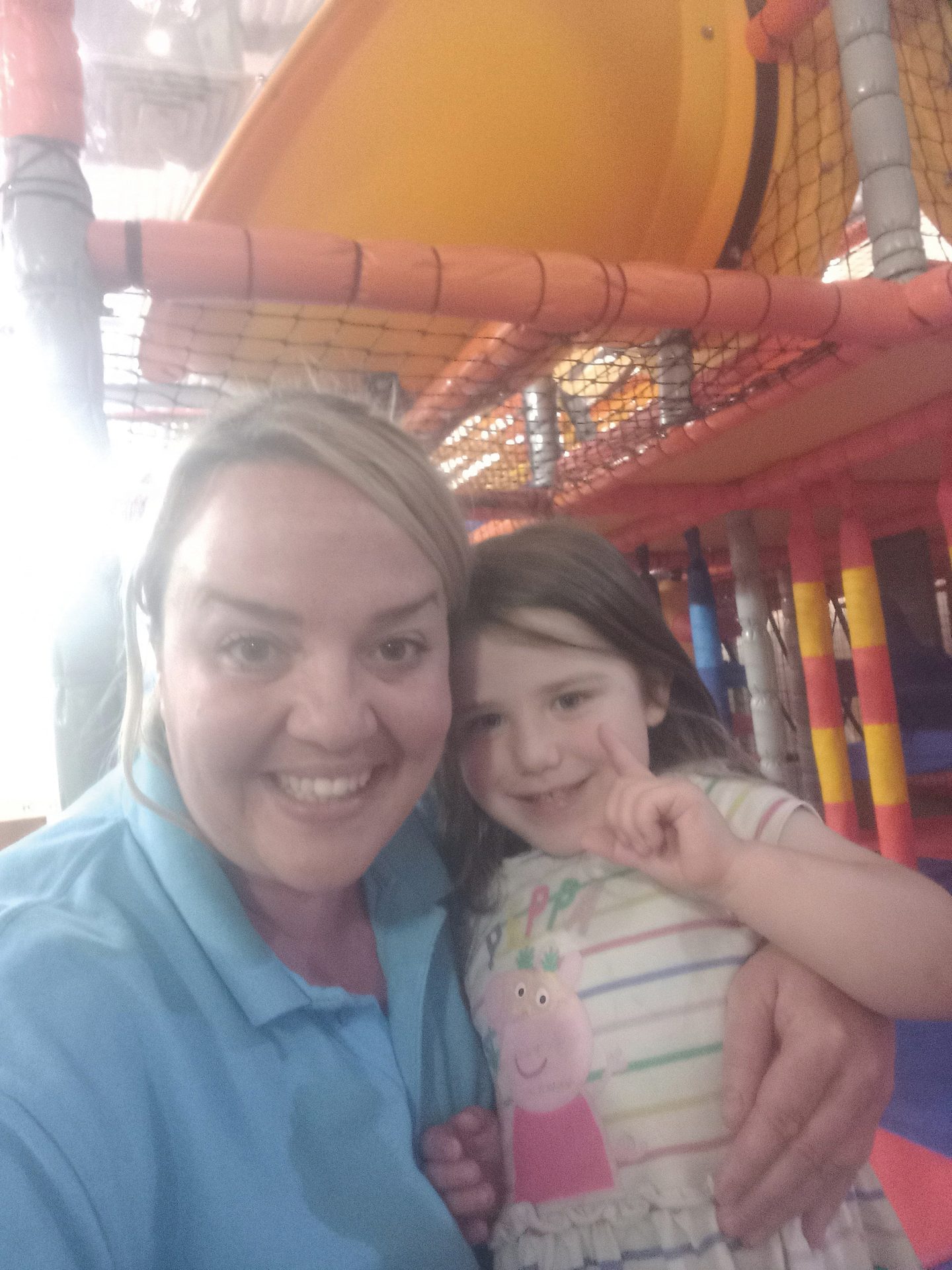 Mother and daughter smiling, posing for a selfie in an indoor playground.