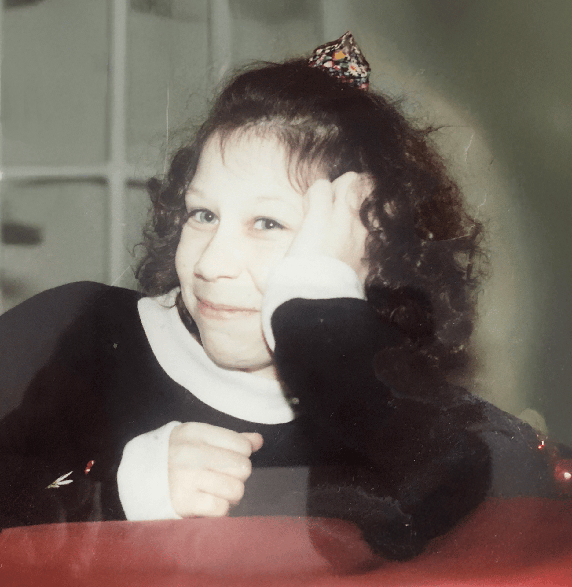Smiling young girl with curly hair and a bow, head resting on her hand.
