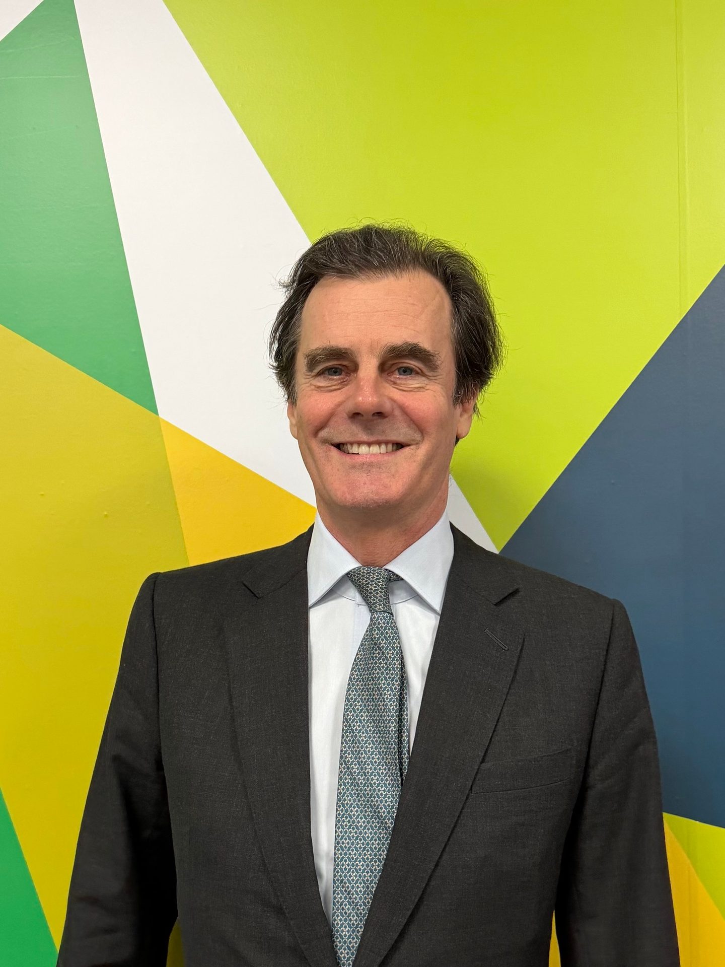 A smiling man in a suit and tie against a colorful geometric background.