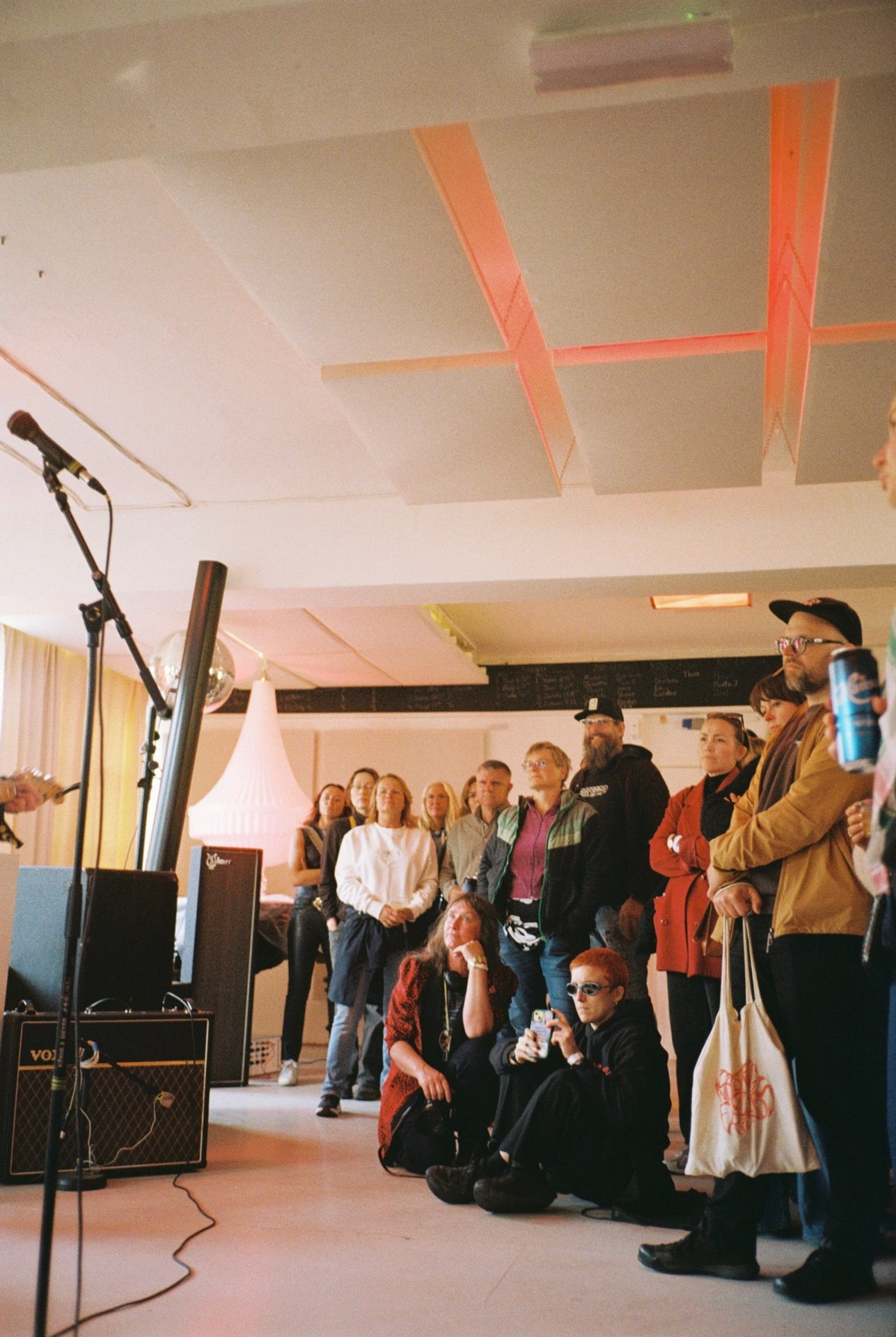 Audience watching an indoor event, with a microphone, speakers, and soundproofing panels visible.
