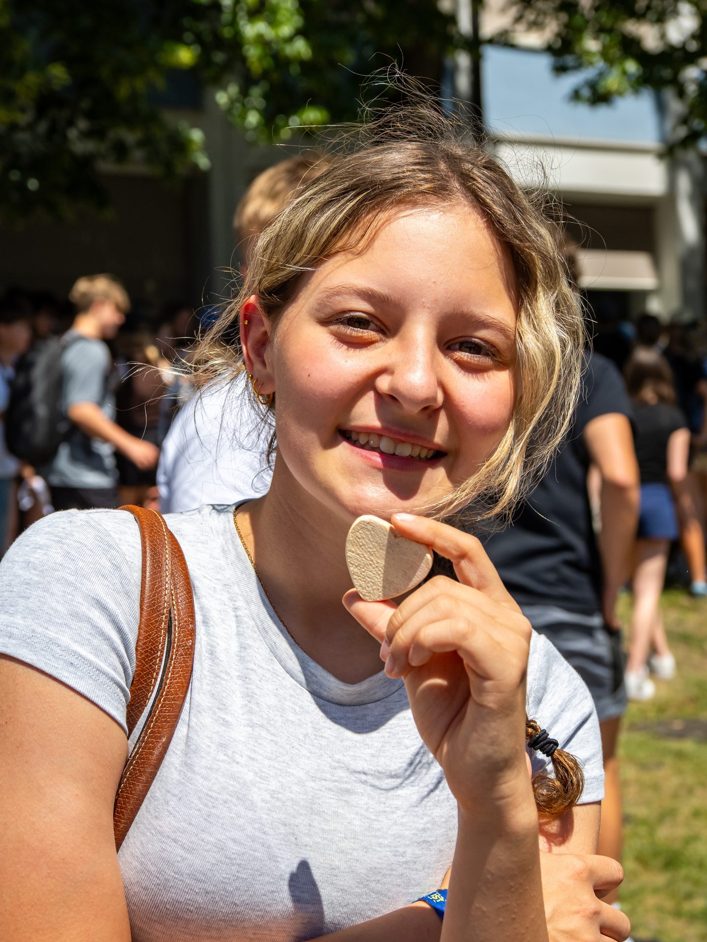 A smiling young woman with blonde hair holds a heart-shaped object, looking directly at the camera.