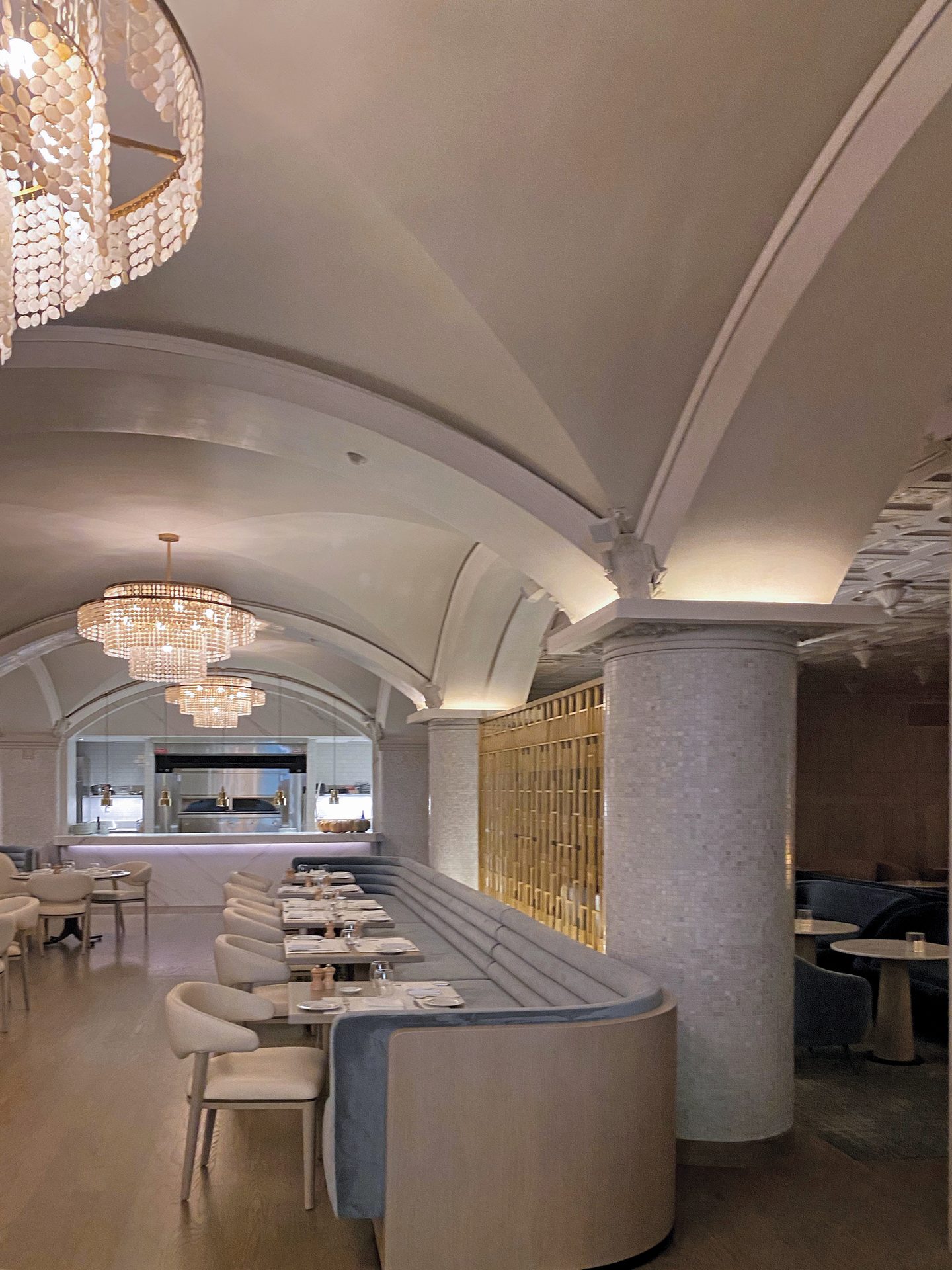 Elegant restaurant interior with vaulted ceilings, chandeliers, banquette seating, and an open kitchen.