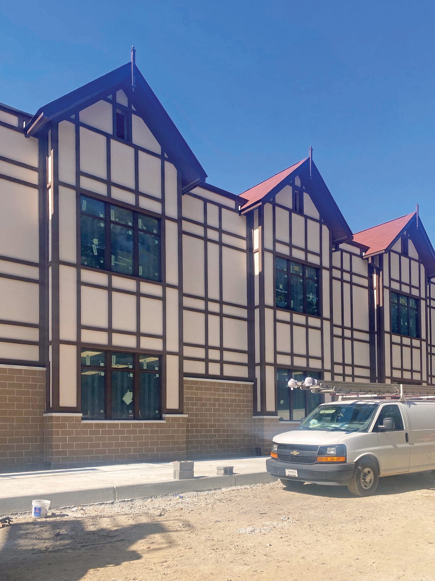 Tudor-style building under construction with half-timbering, red gables, and a white construction van.