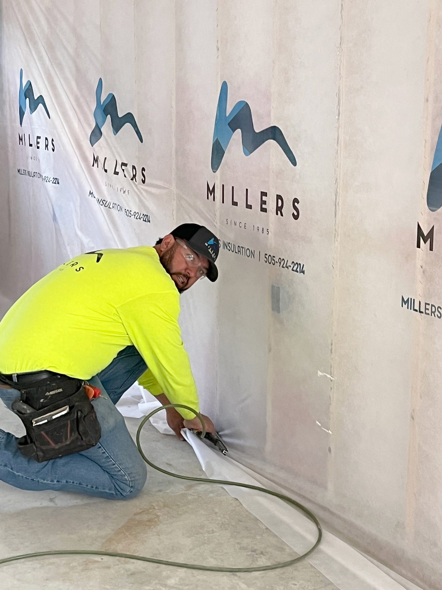 Man kneels, installing insulation on a wall branded "Millers Insulation."