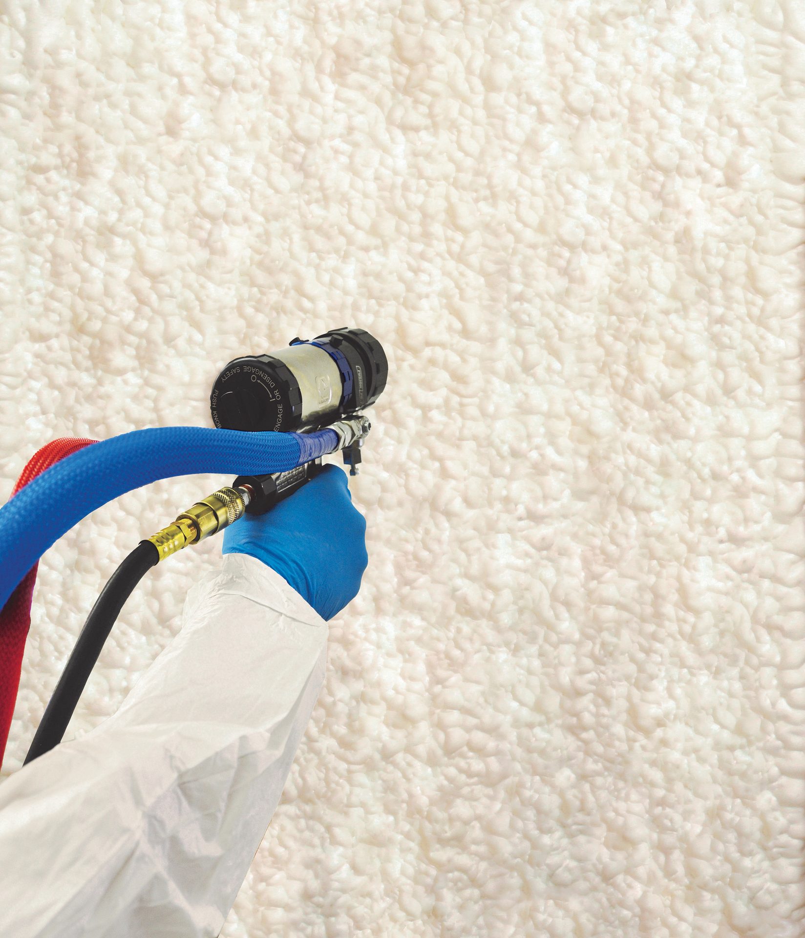 A hand in a blue glove sprays cream foam insulation onto a wall with a spray gun.