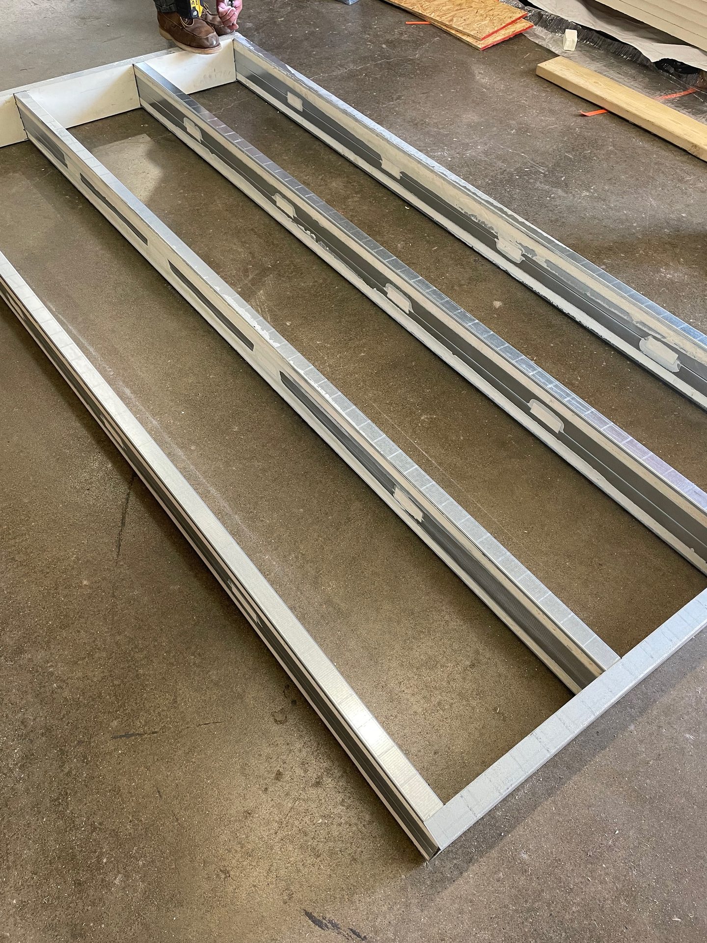 Metal frame with three parallel channels, lined with dark gray strips, on concrete.