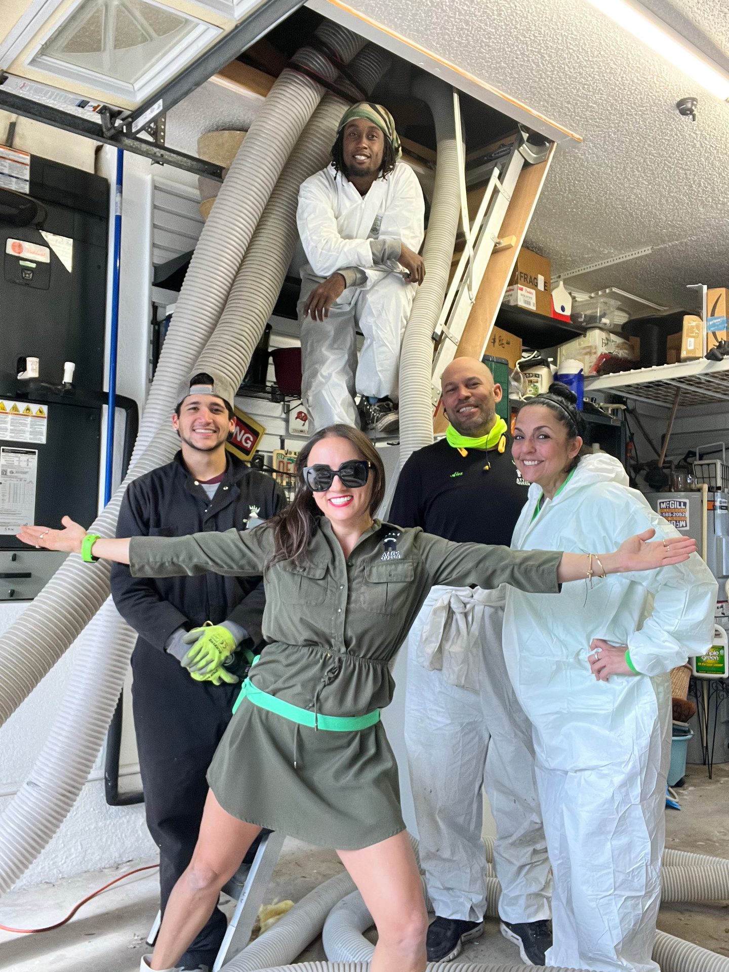 Five people, some in protective suits, pose in a garage with insulation hoses.