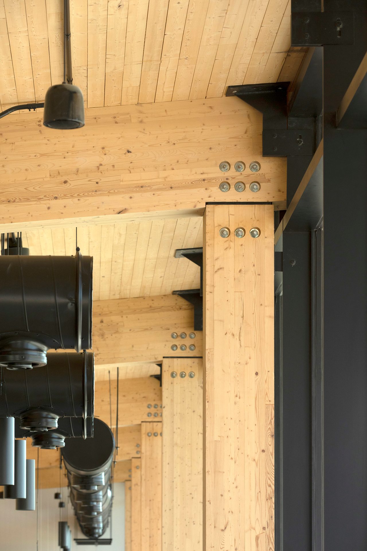 Close-up of a modern timber and steel structural system with exposed ducts and wooden ceiling panels.
