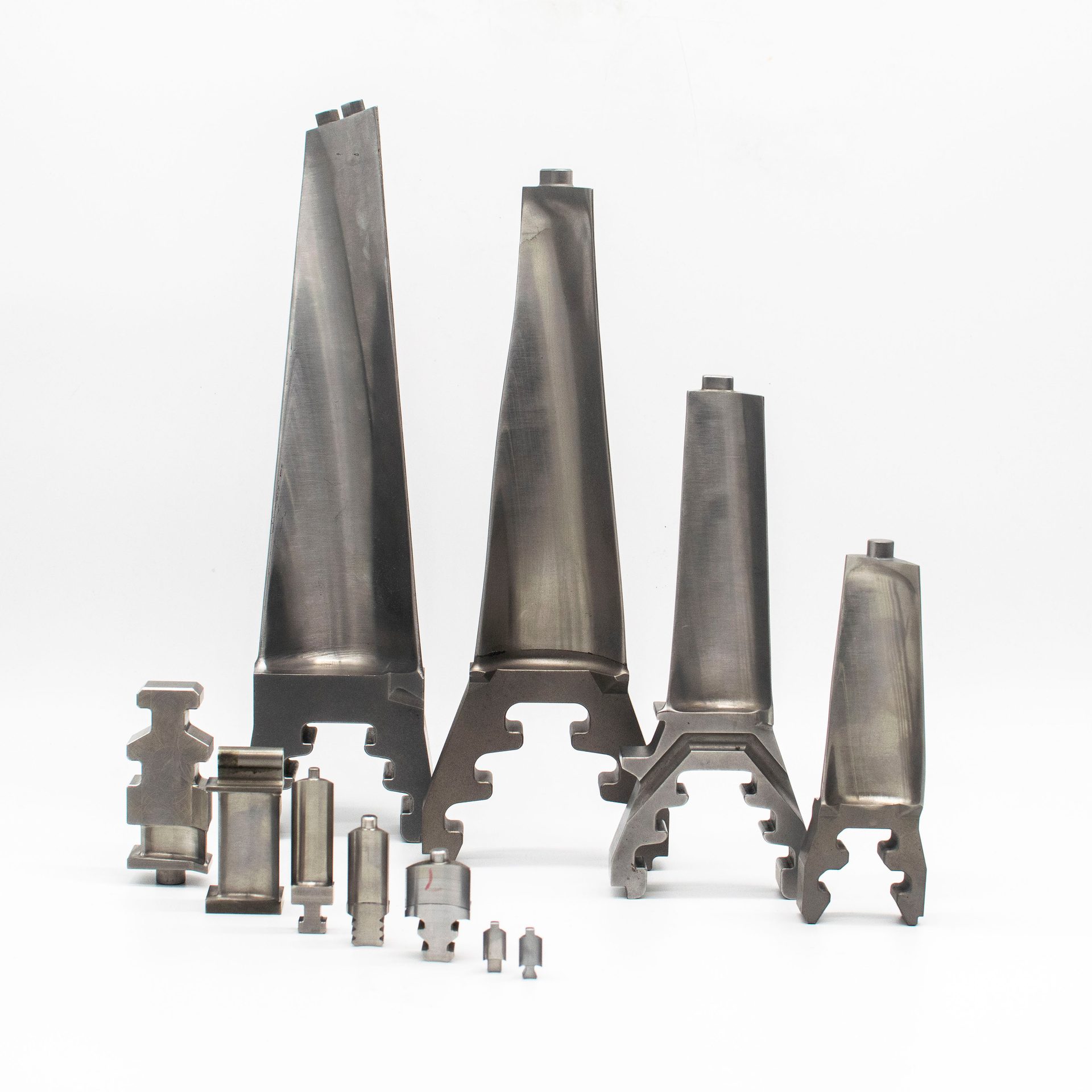 A collection of metallic turbine blades and smaller precision-engineered industrial parts on a white background.