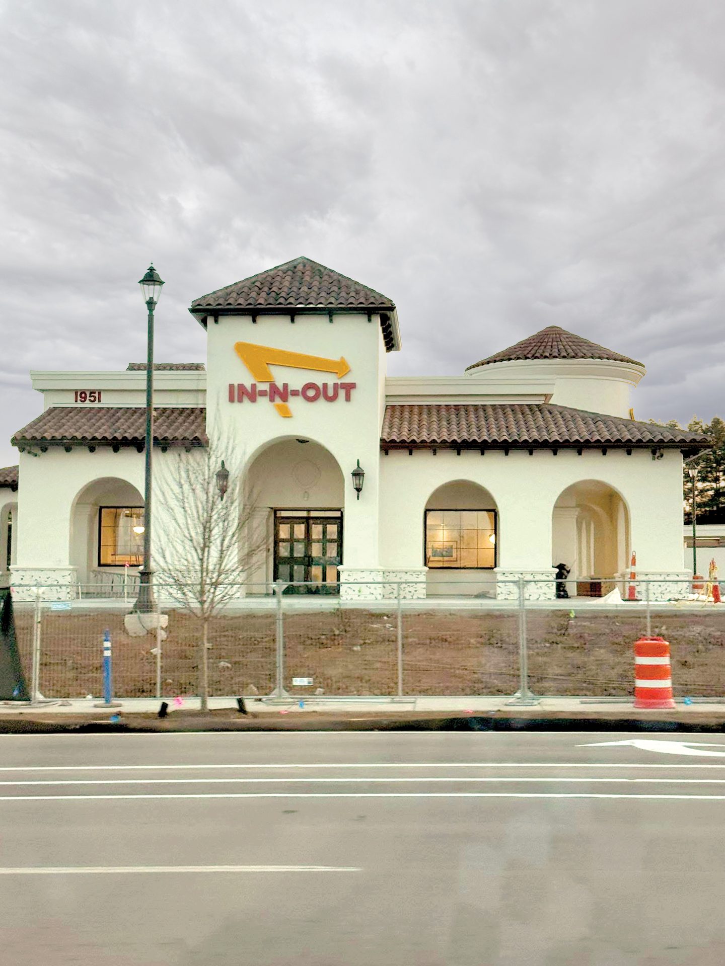Spanish Colonial In-N-Out Burger restaurant, under construction with a fence, under a cloudy sky.