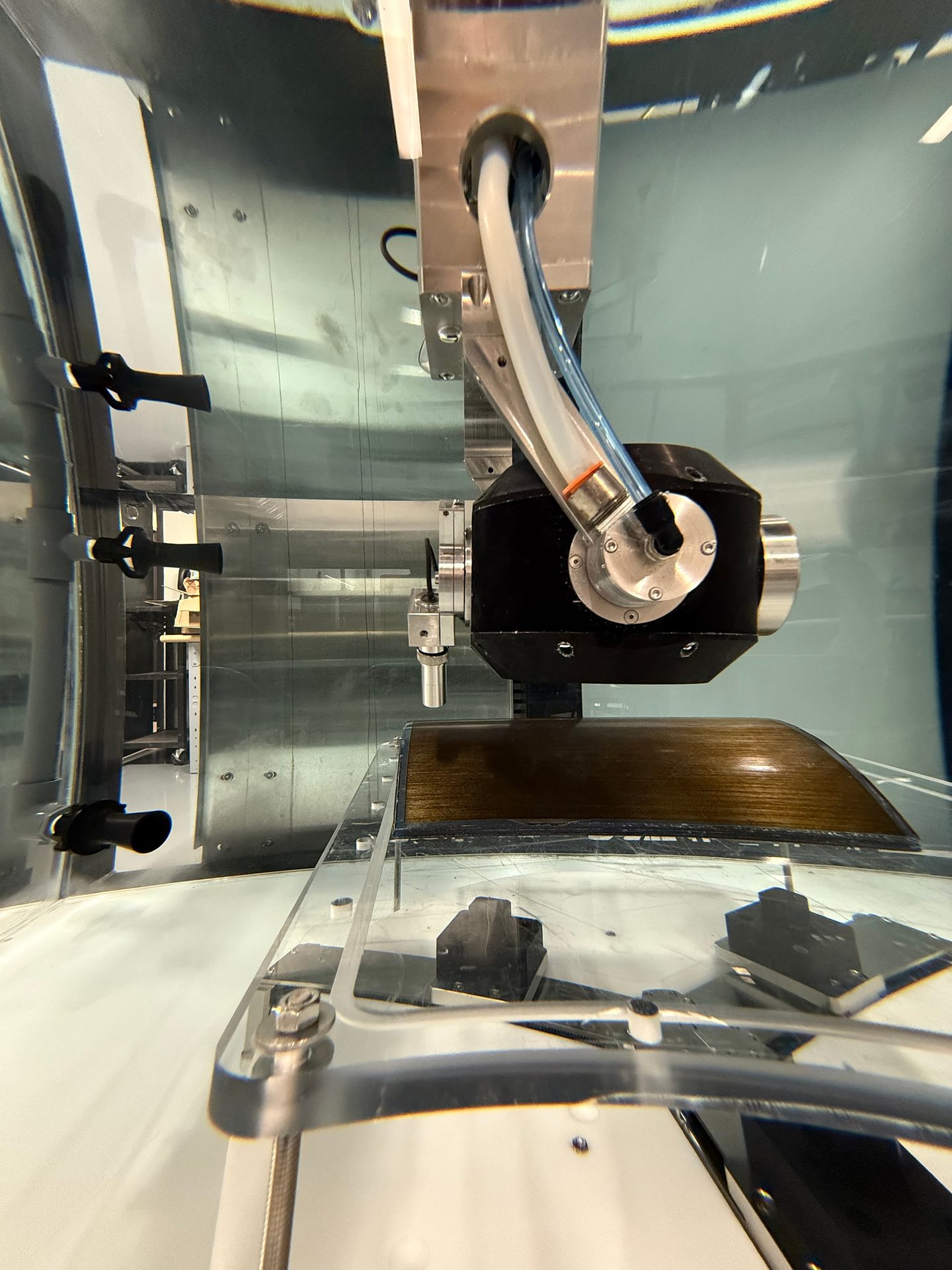 Robotic arm with hoses submerged in a clear tank over a textured object.