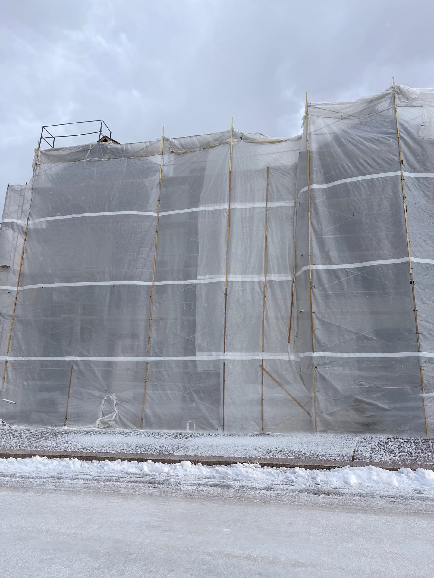 Building under renovation covered in white plastic wrap and scaffolding, with snow on the ground.