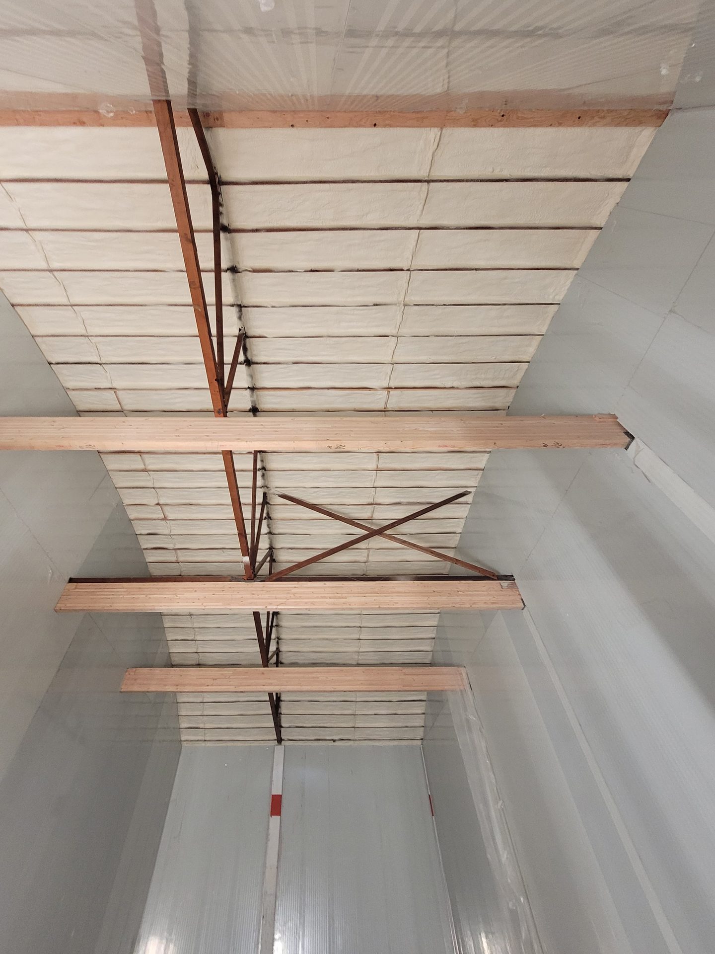 Interior of a building with insulated ceiling panels and exposed wooden beams and trusses.