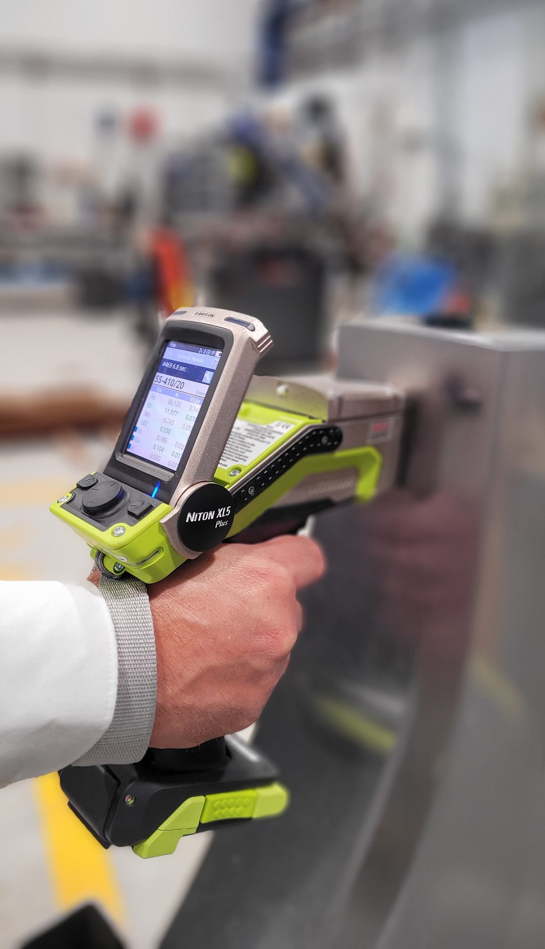 Handheld Niton XL5 Plus XRF analyzer scanning a metal object, showing elemental data.