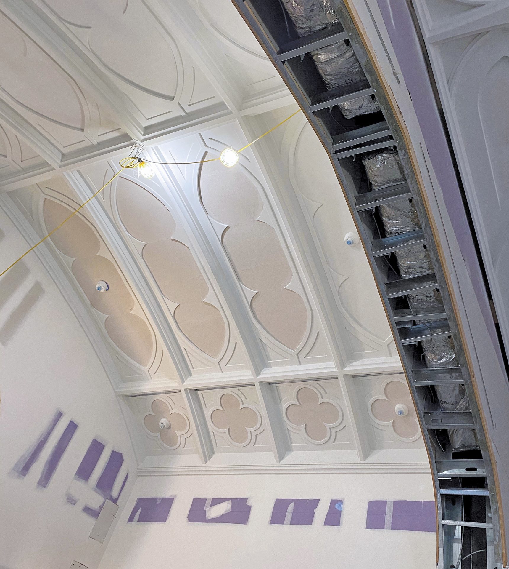 Ornate ceiling plasterwork contrasts with exposed metal framing and ductwork in a renovation.