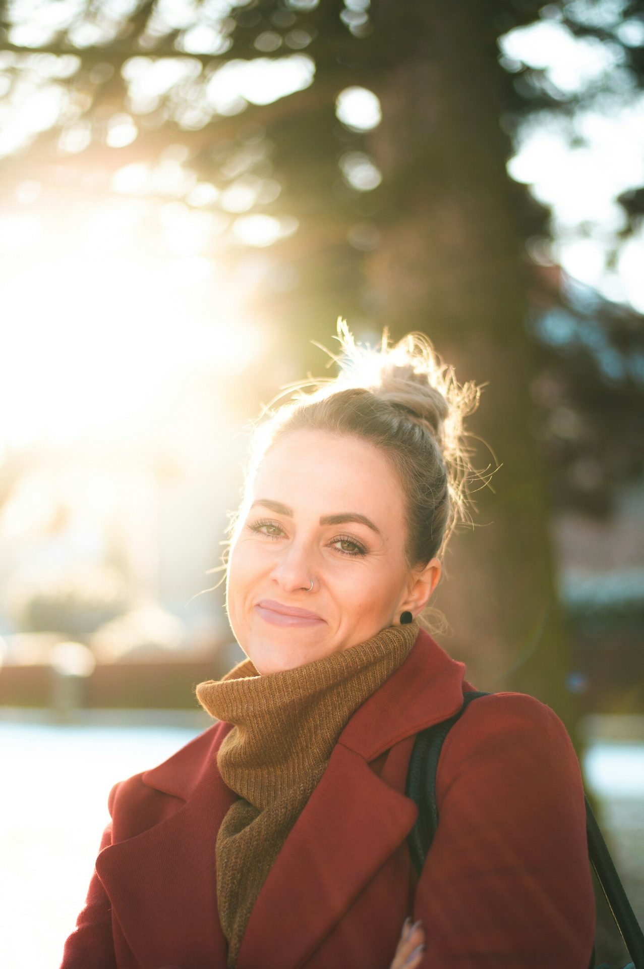 Happy woman in a red coat and brown turtleneck, backlit by golden sunlight.