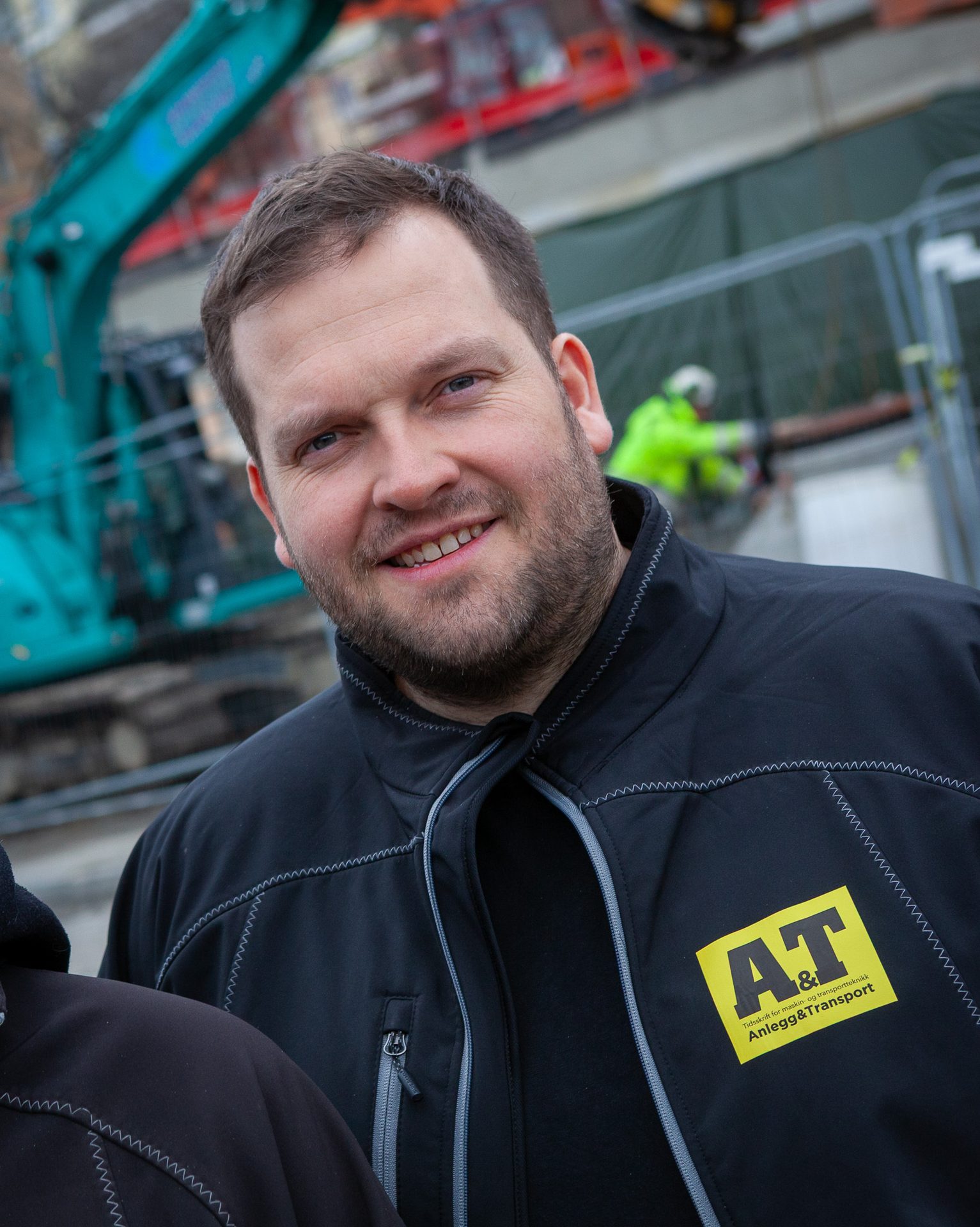 Smiling man in black A&T jacket at a construction site.