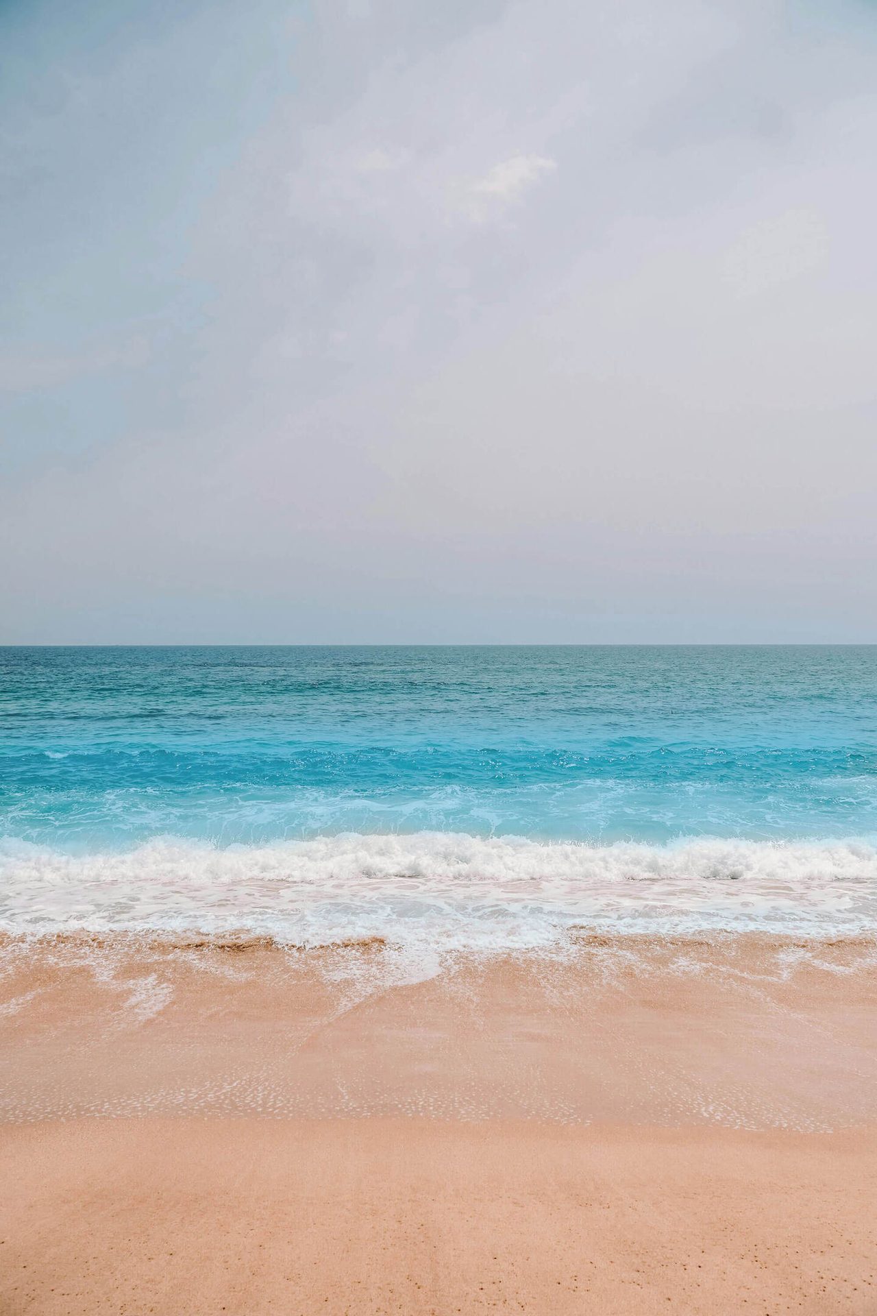 Sandy beach, turquoise ocean waves, and a pale sky.