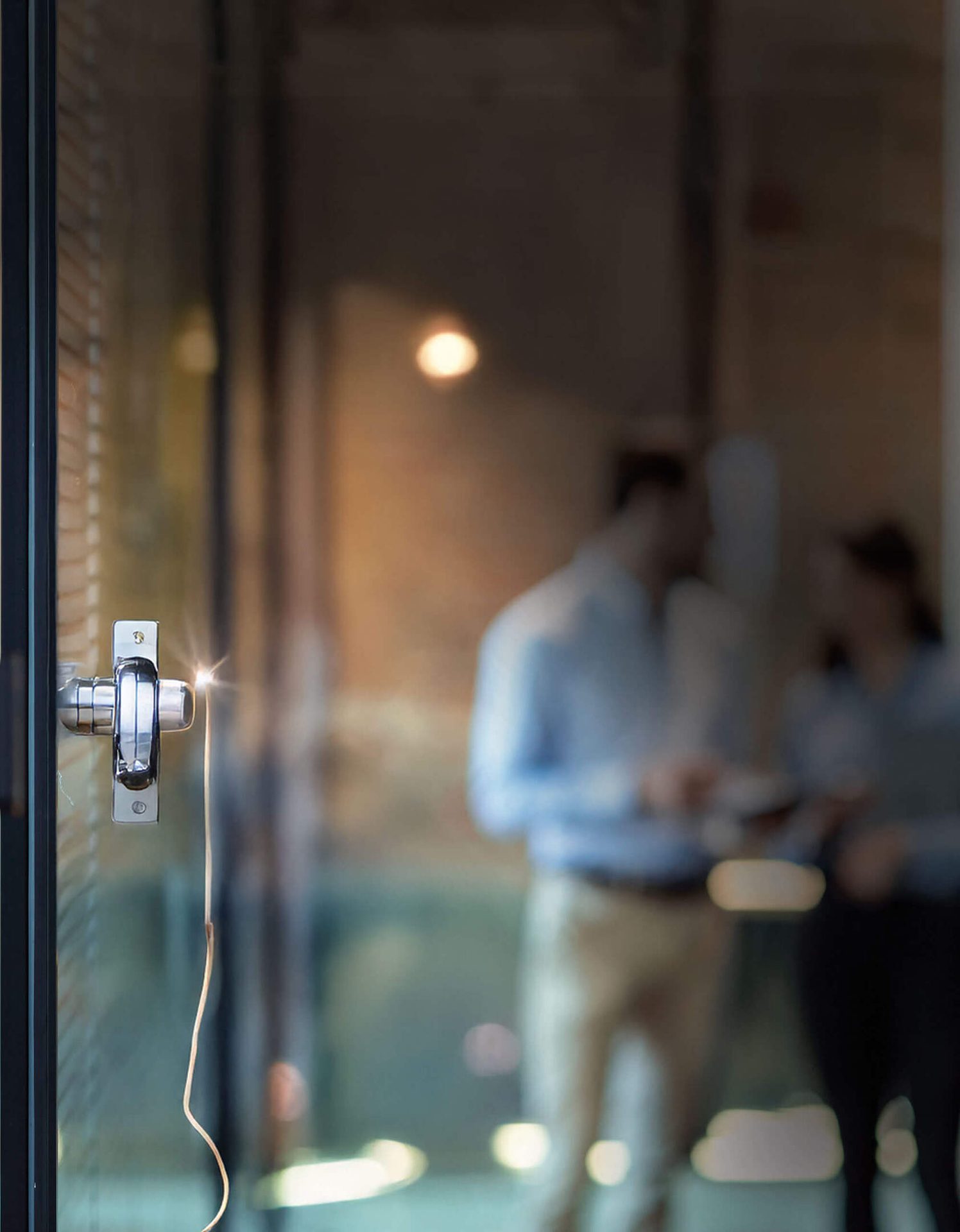 Reflective glass door with a shiny handle and wire, showing blurred figures inside.
