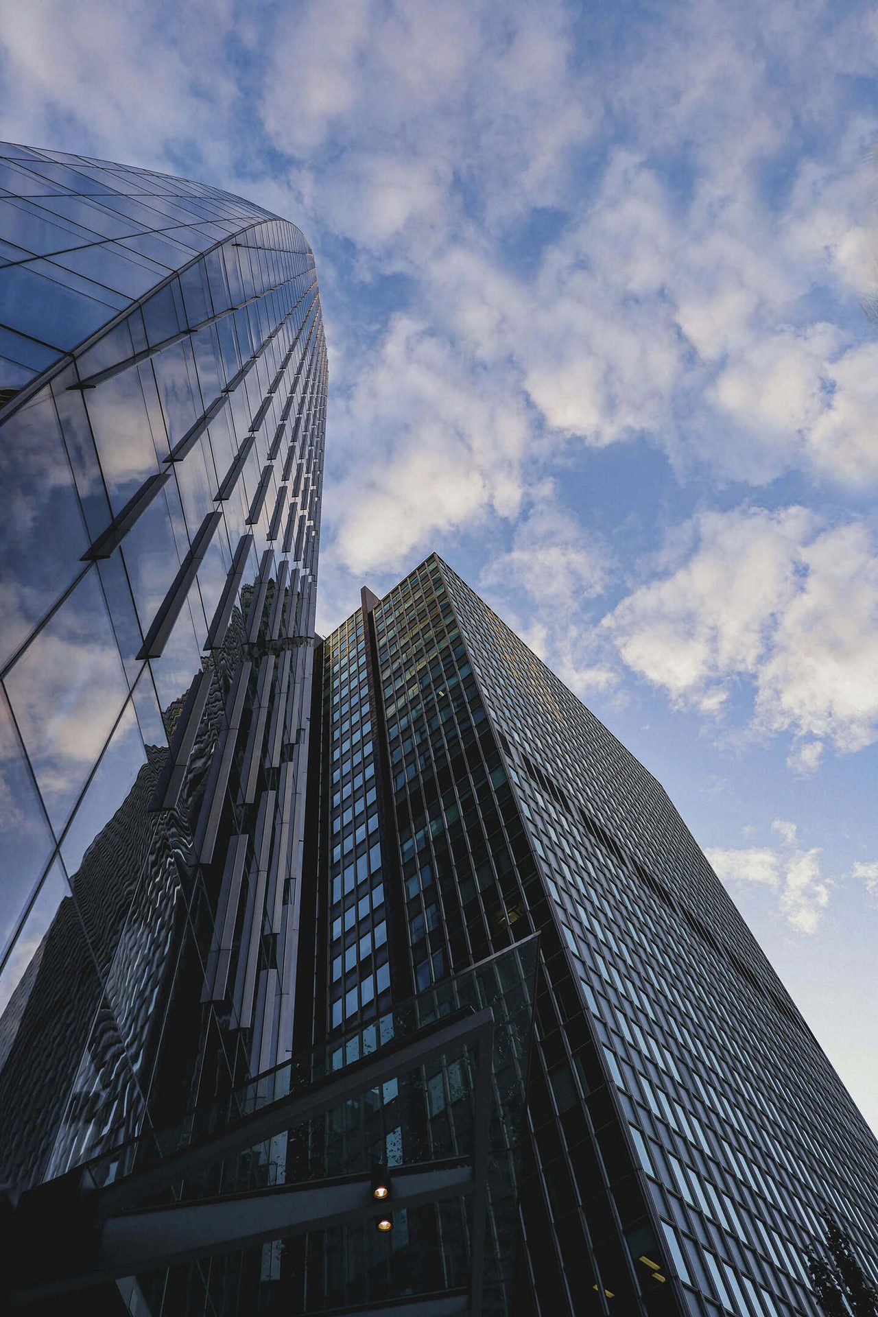 Modern glass skyscrapers reaching into a cloudy blue sky, captured from a low angle.