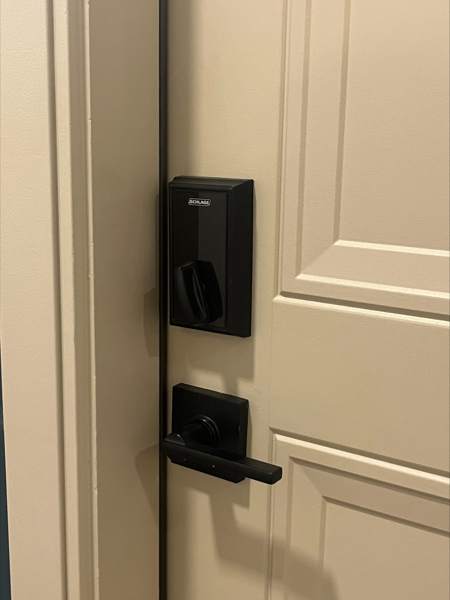 A cream-colored door features a black Schlage smart lock and a matching lever handle.